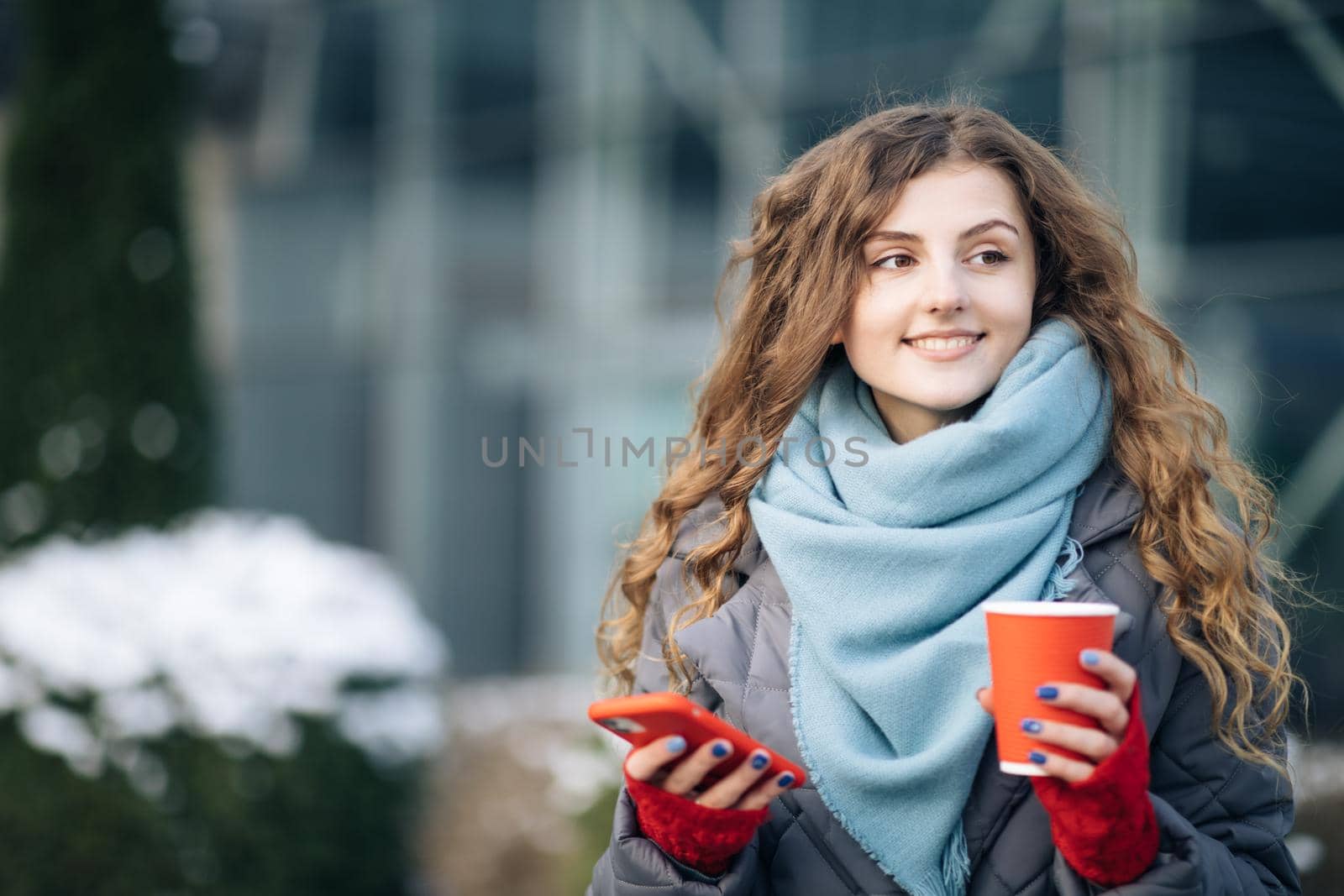 Portrait of happy beautiful curly woman with coffee cup takeaway use mobile phone texting messages. Walking look around on the street city.