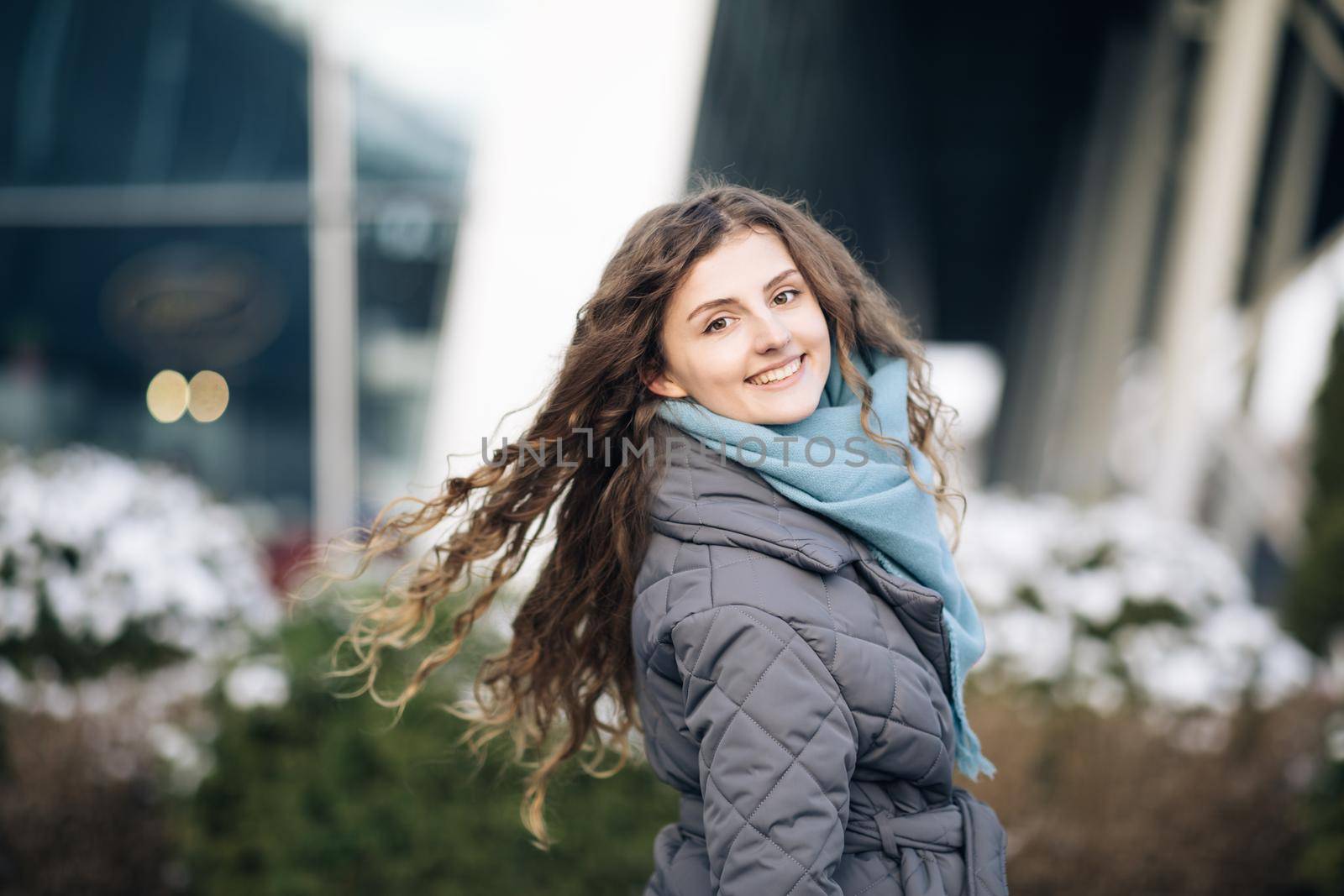 Beautiful caucasian elegant girl with beautiful curly brown hair walks happy in downtown. Happy Young Woman Enjoys Life. Amazing young cheerful curly female model walking on street posing for camera. by uflypro