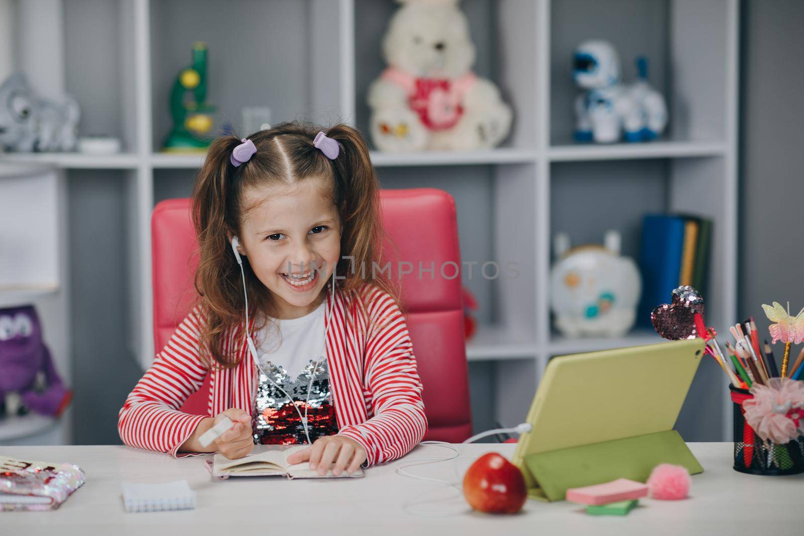 Distance learning, school online. Portrait of a preschool girl looking at the book and smiling. Self isolation and online schooling