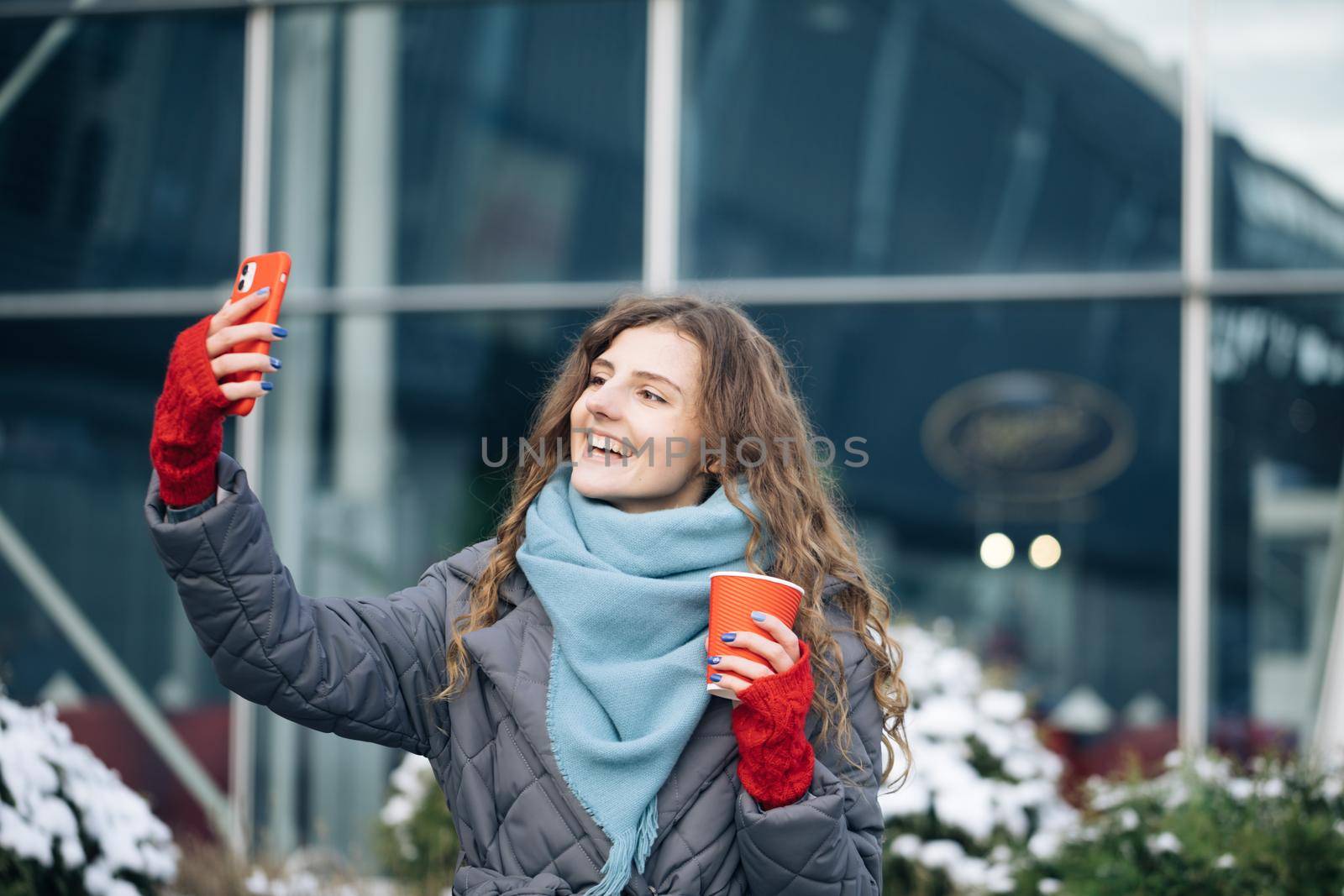 Portrait of happy girl taking selfie holding camera at city street. Modern technology, lifestyle and joyful people concept.