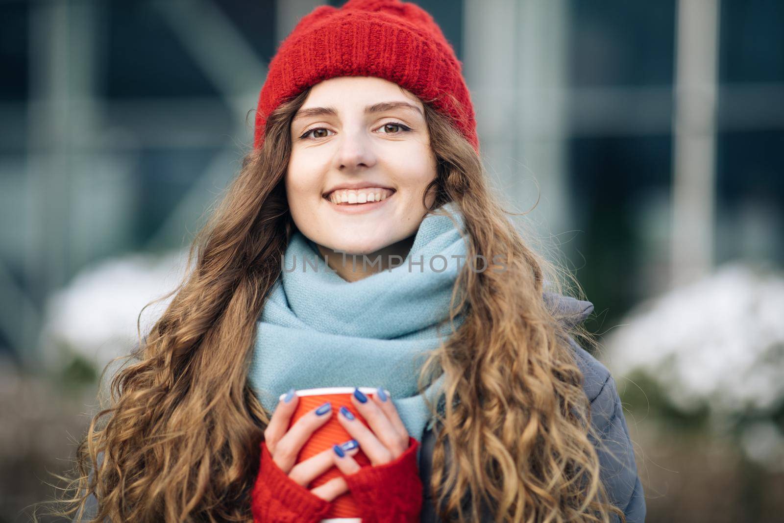 Cheerful gorgeous curly brunette in winter fashion holding coffee cup on urban background. Concept happiness, winter holidays, christmas, beverages and people. Curly female standing on winter street by uflypro