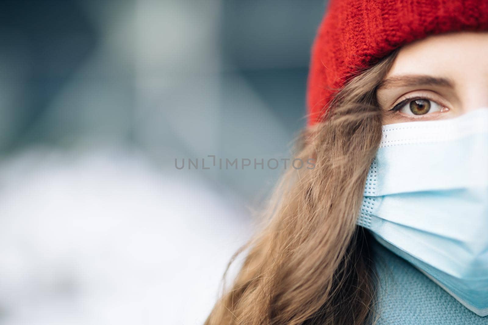 Close up of female half face at street . Portrait of caucasian woman looking at camera. Curly haired woman wears protective mask to avoid contaminating coronavirus. Health and safety concept.
