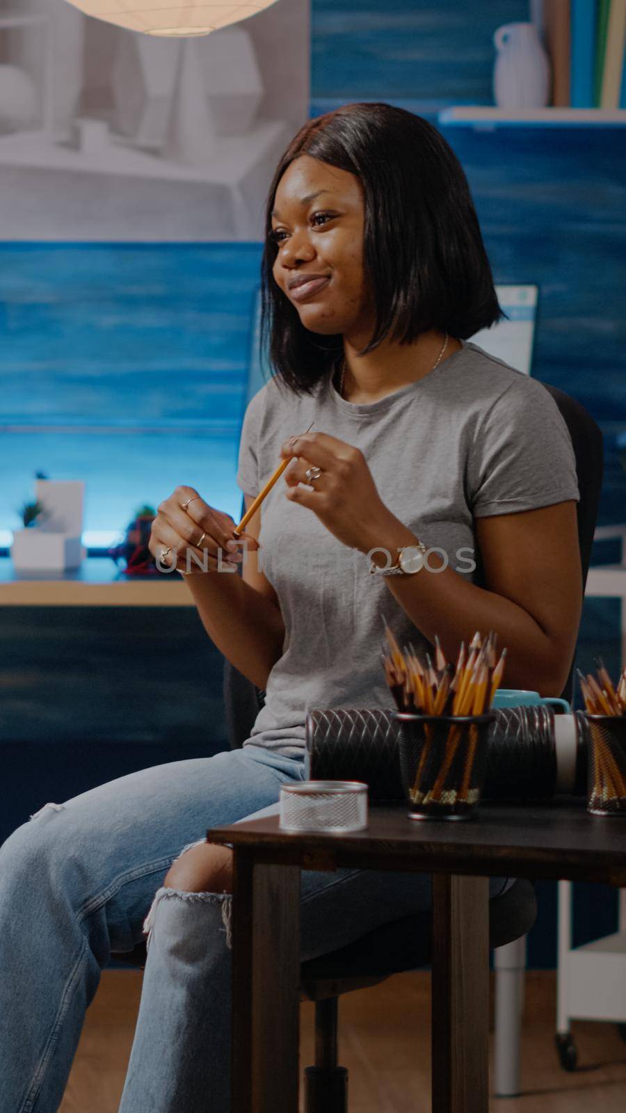 Black artist woman sitting at studio with canvas and easel and drawing. African american young adult using pencil for masterpiece creation art fine art concept. Person with creativity