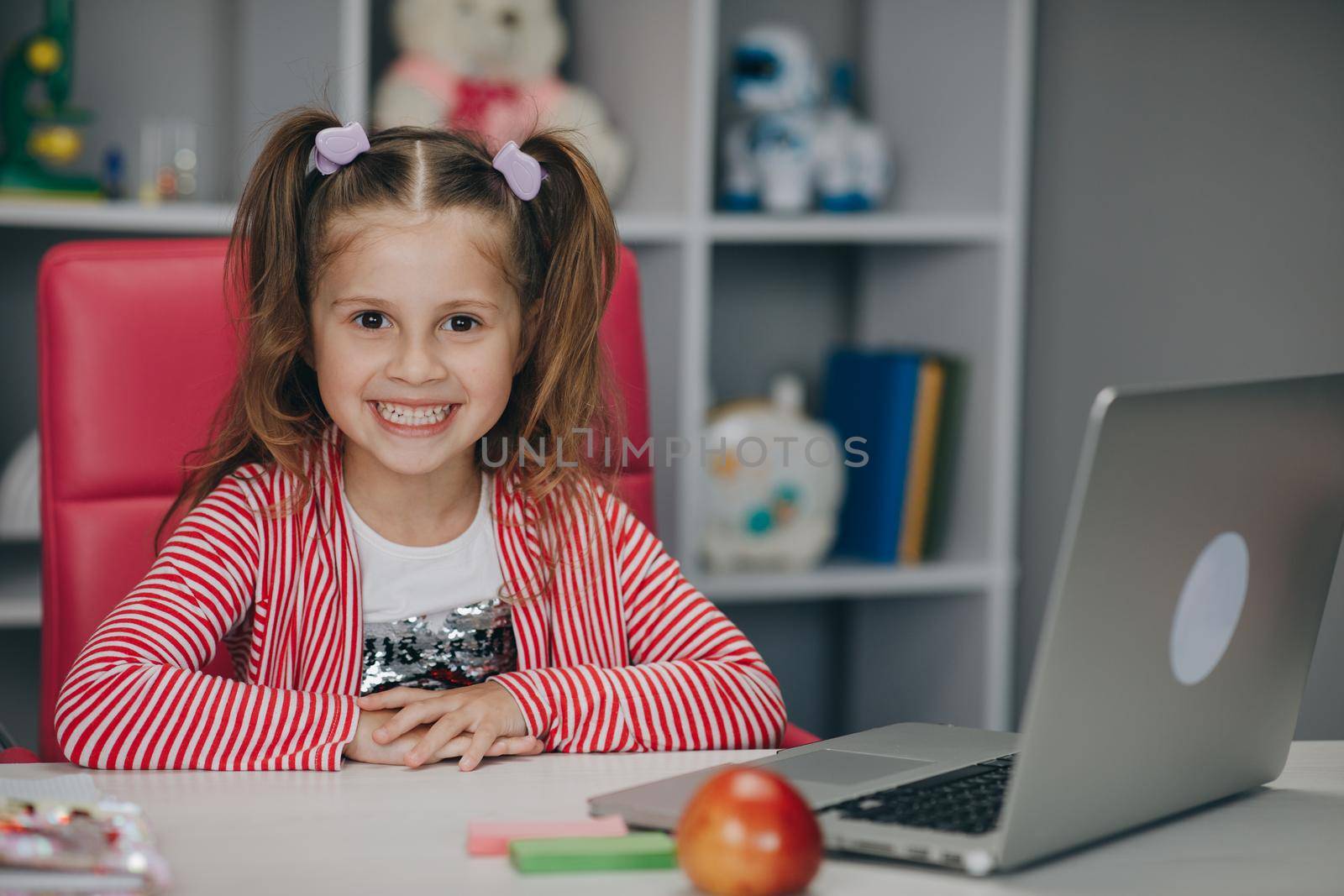 Smiling adorable elementary school age child learning class alone sitting at table with laptop. Cute kid girl doing homework.