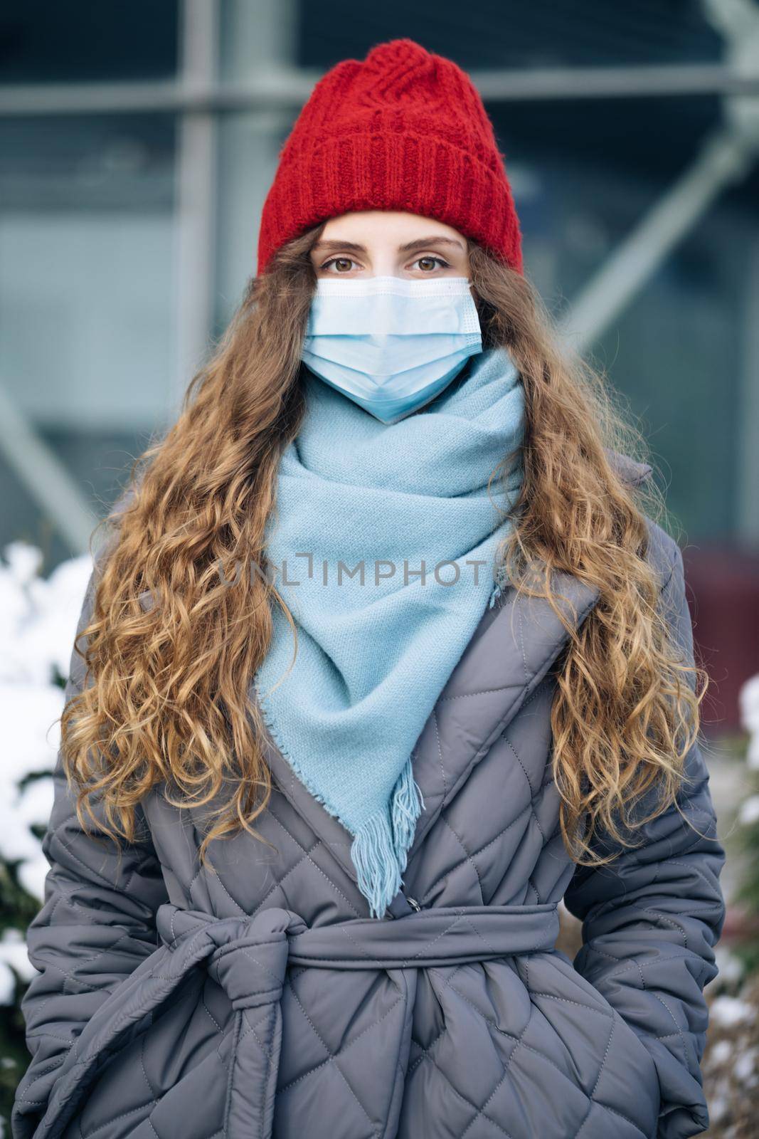 Portrait of a woman with curly hair in the city streets during the day, wearing a face mask against air pollution and Coronavirus Covid19 , looking at camera.