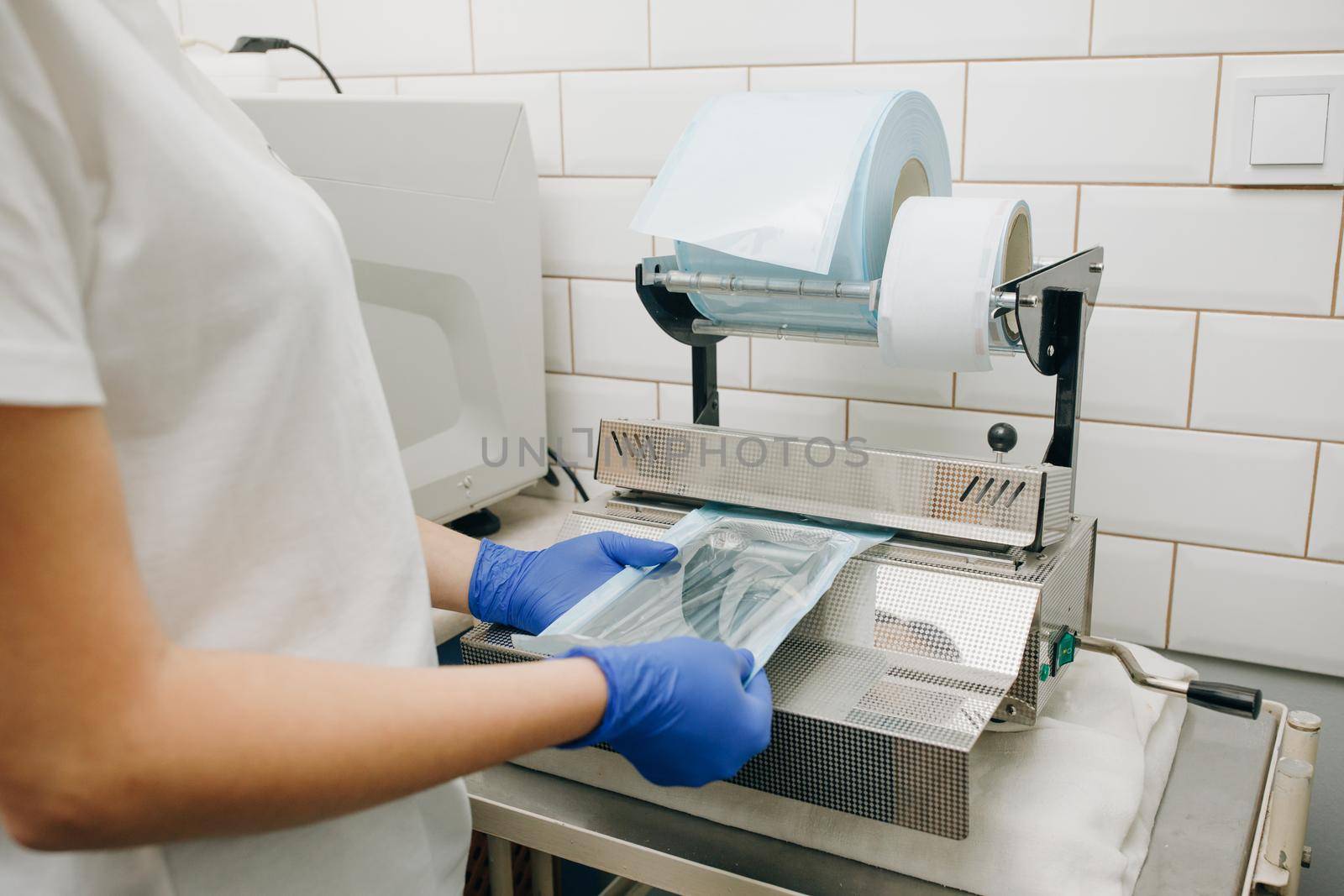 Dentist's assistant hands in gloves packing dental instrument set for autoclaving in a plastic bag using vacuum packing machine. Sterility and safety care concept