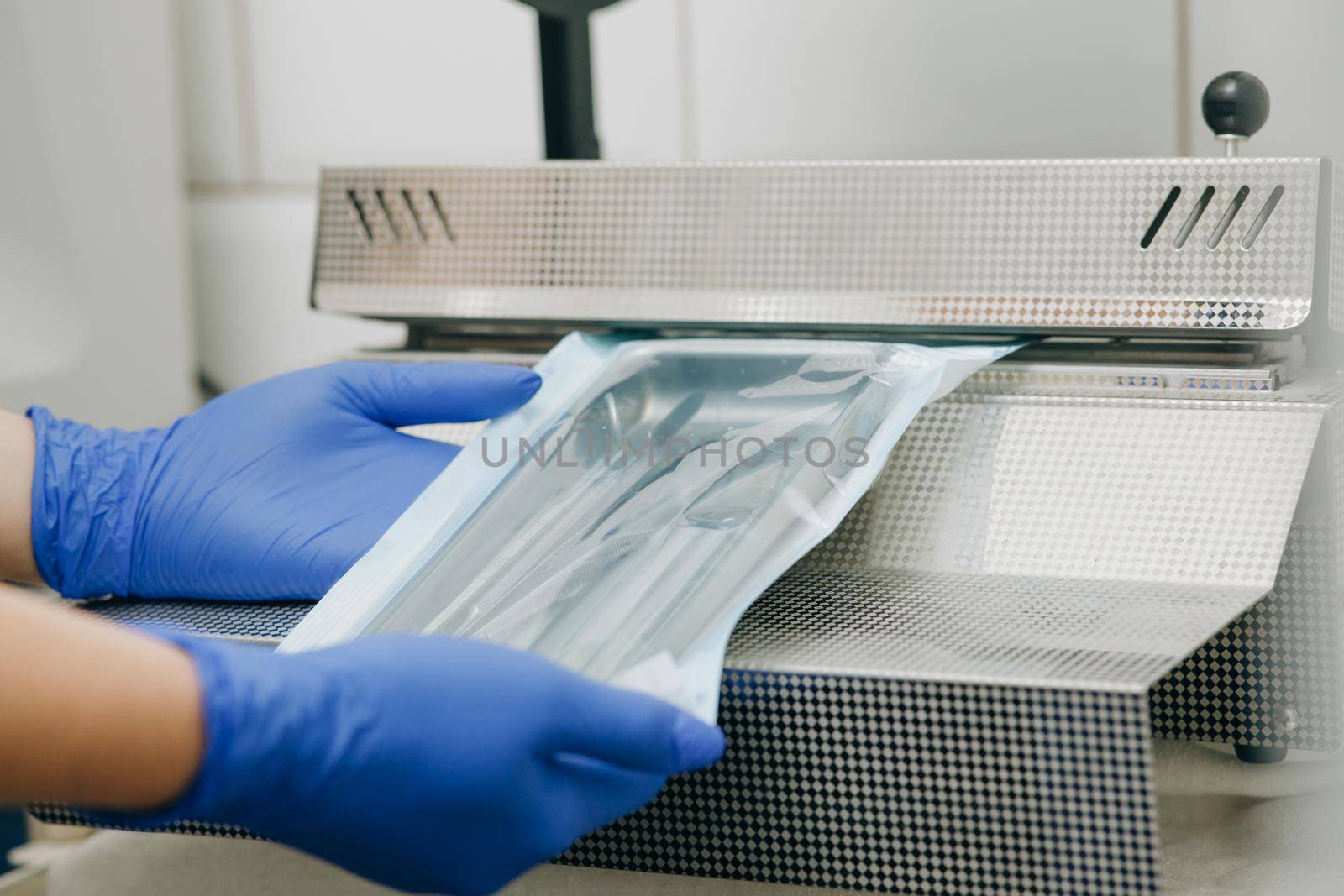 Close up dentist's assistant hands in gloves packing dental instrument set for autoclaving in a plastic bag using vacuum packing machine. Sterility and safety care concept. by uflypro