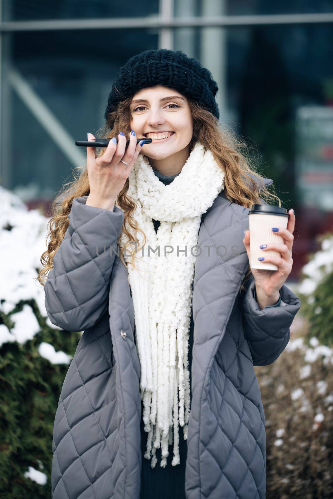 Portrait of Curly haired Woman with phone using the voice recognition ai audio message on the phone, audio message ai speech helper. Vacation winter outdoor.