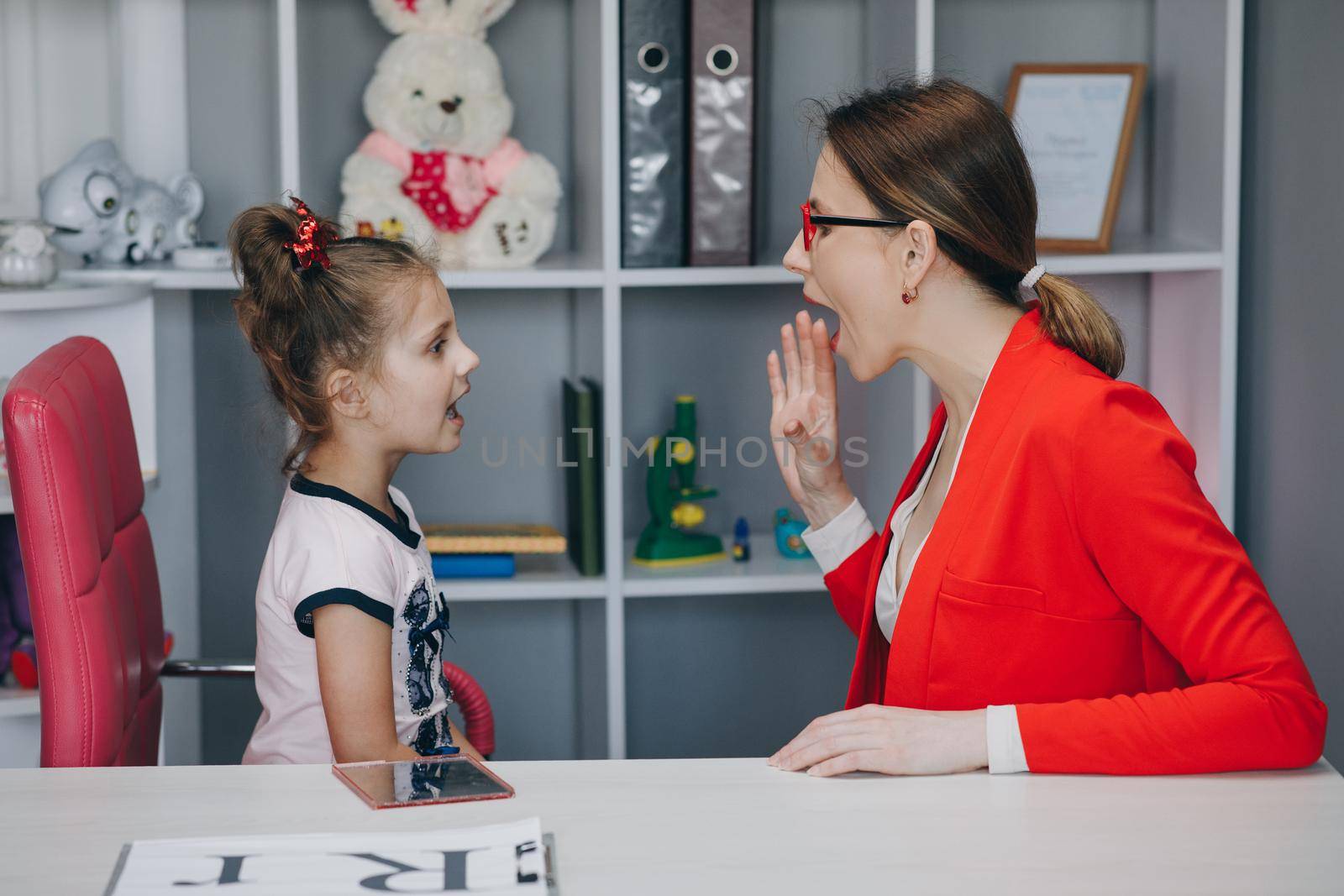 Cute little girl at speech therapist's office. Small child practicing articulation with therapist at private lesson at home.