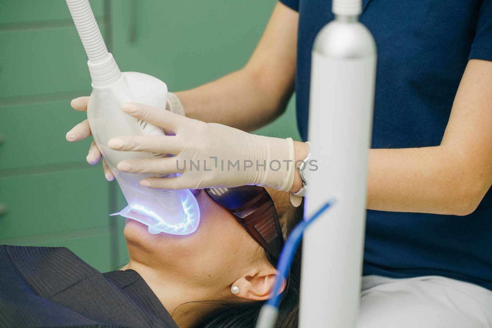 Teeth whitening procedure. Dentist stomatologist whitening teeth for patient in medicine dental clinic with lamp. Powerful light source is directed at patient's mouth to speed up the process. by uflypro