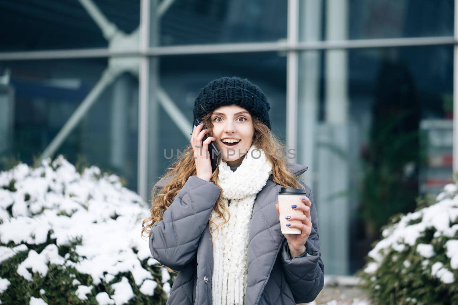 Excited woman winner screaming yes rejoicing success at cellphone. Portrait of young curly woman in winter clothes holding phone celebrate good mobile news surprise bid by uflypro