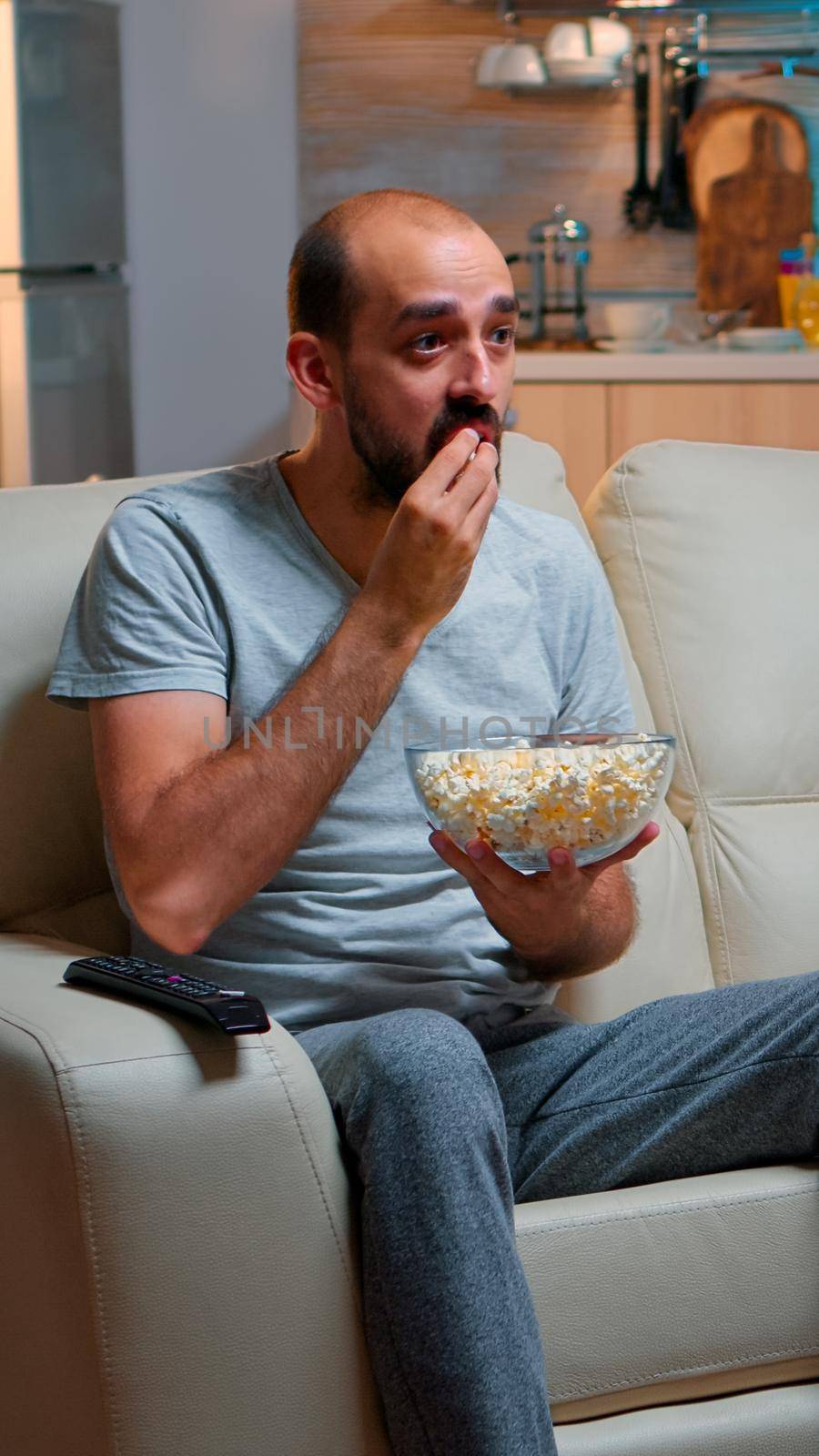 Sport football fan watching game late at night while enjoying popcorn, cheering for favourite football team. Championship entertainment match alone television, soccer fan looking at competition