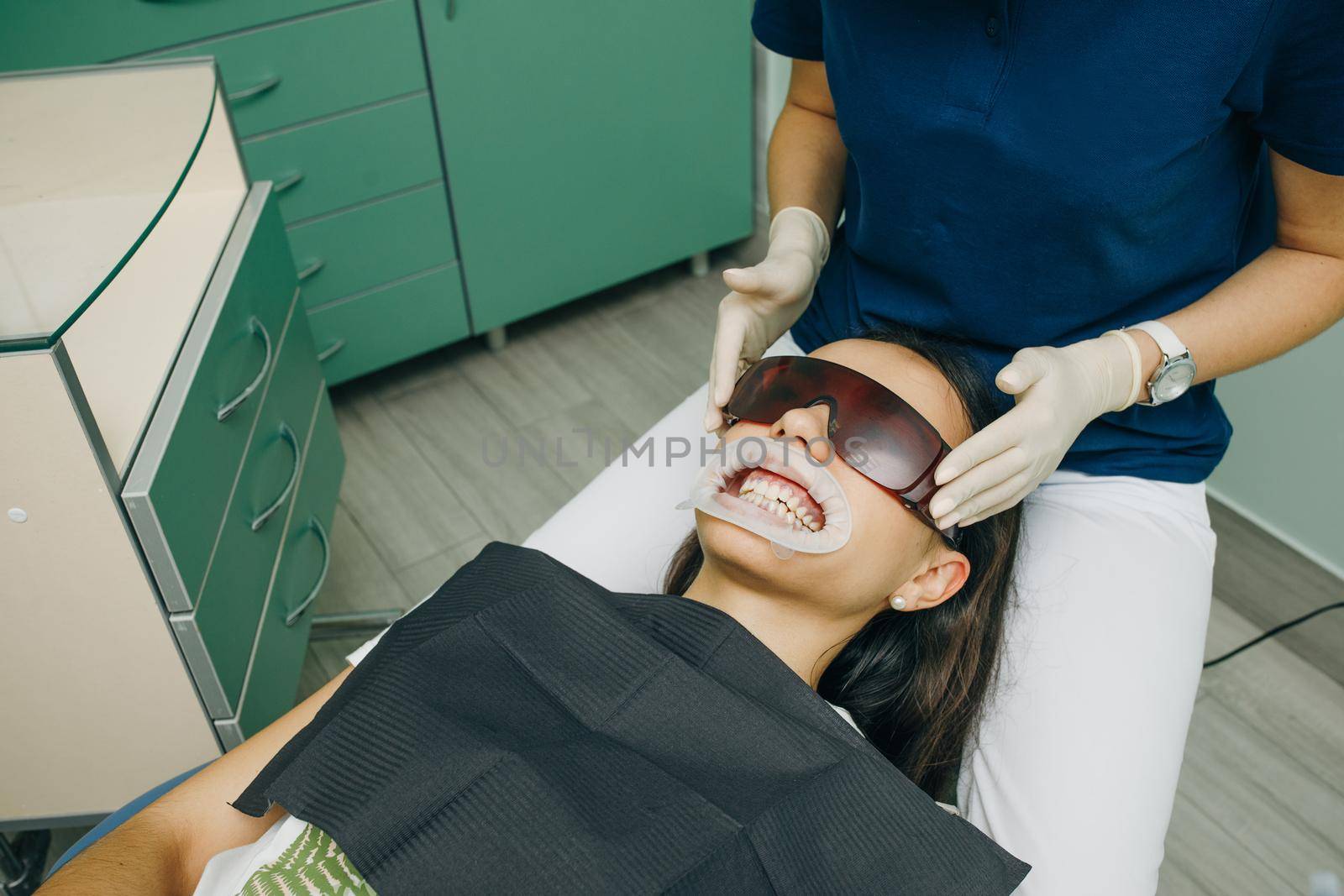 Female client of a clinic sits with his mouth open in a dental chair, wearing orange safety glasses. Dental office. Dentistry. Stomatology.