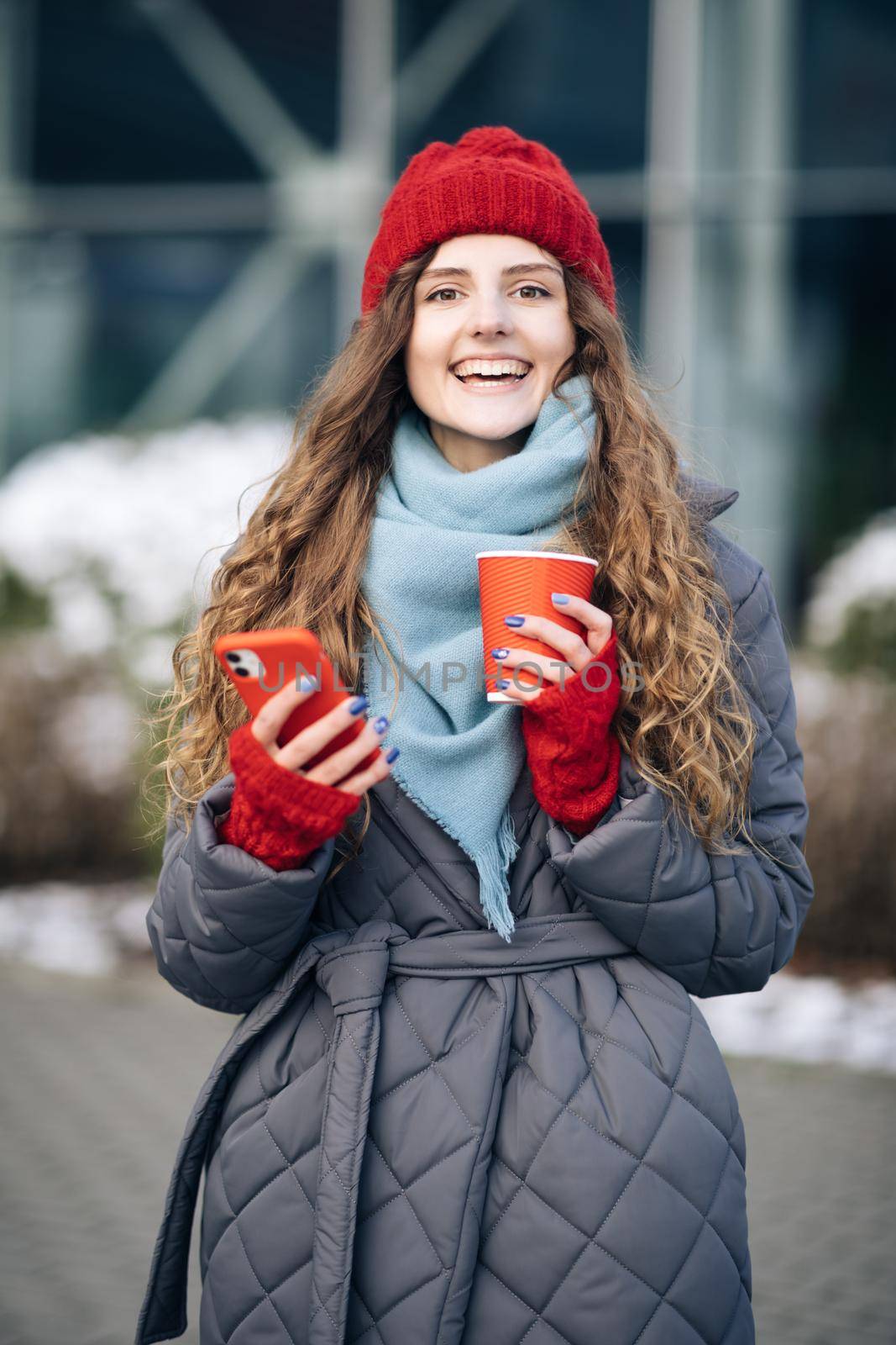 Female look around on the street city. Modern stylish curly woman with cup coffee, uses her smartphone . Being online, social networks by uflypro