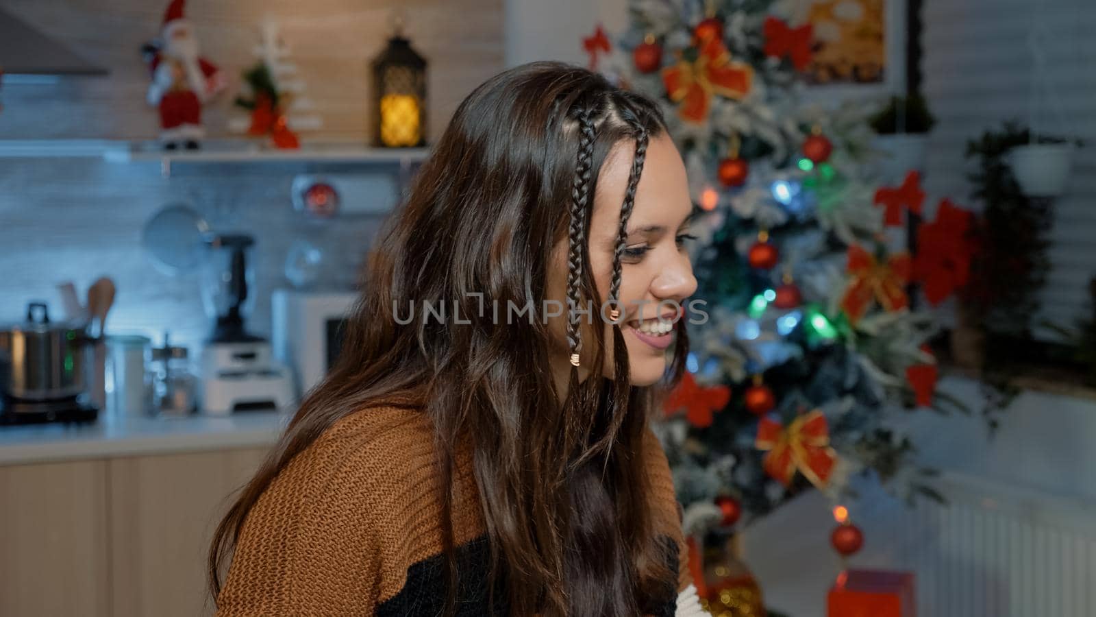 Young woman using modern technology for video call communication with friends in festive kitchen. Caucasian person making preparations on laptop for christmas day dinner celebration