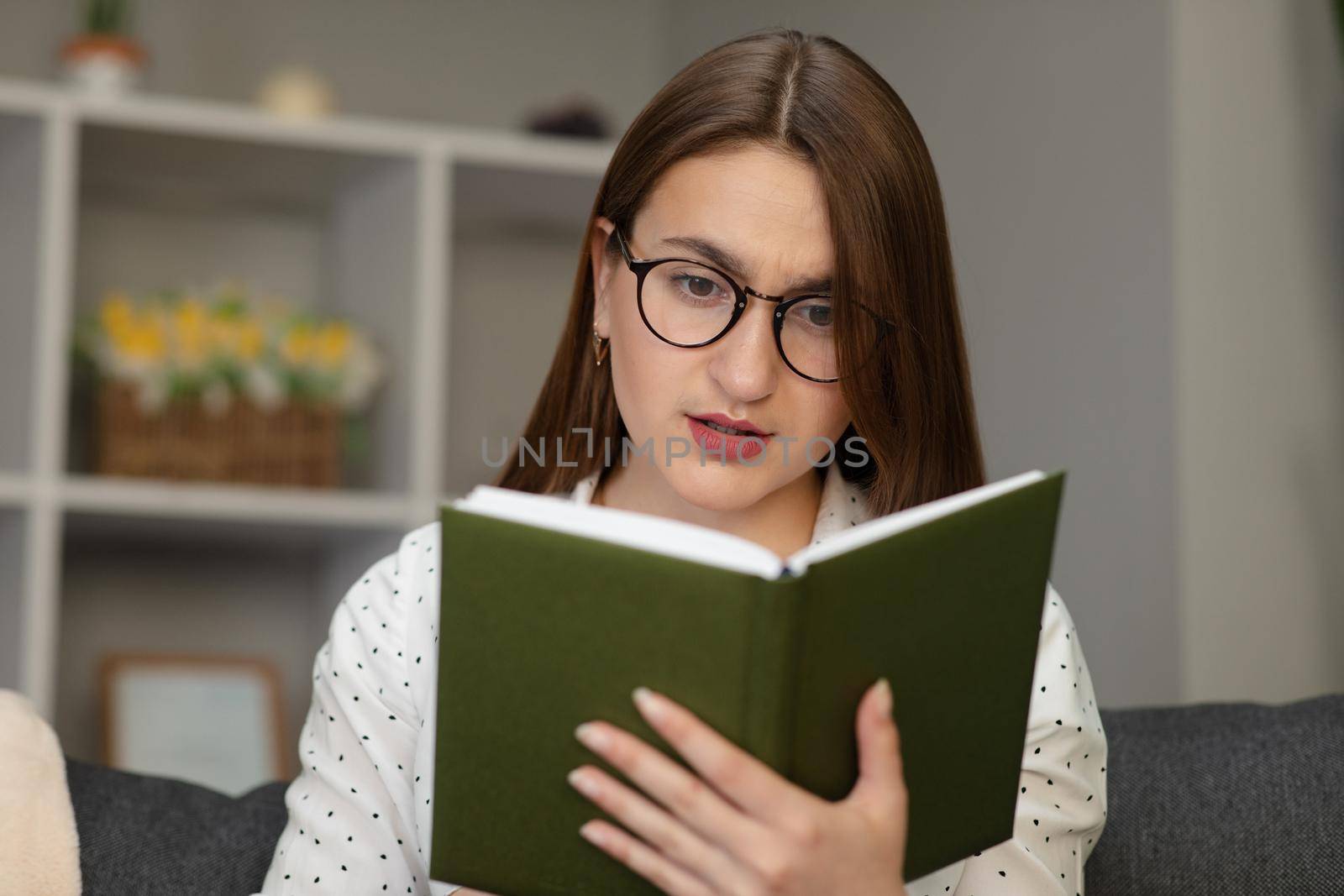 Portrait of a young student reading a book. Beautiful young brunette woman reading a book on the bed at home