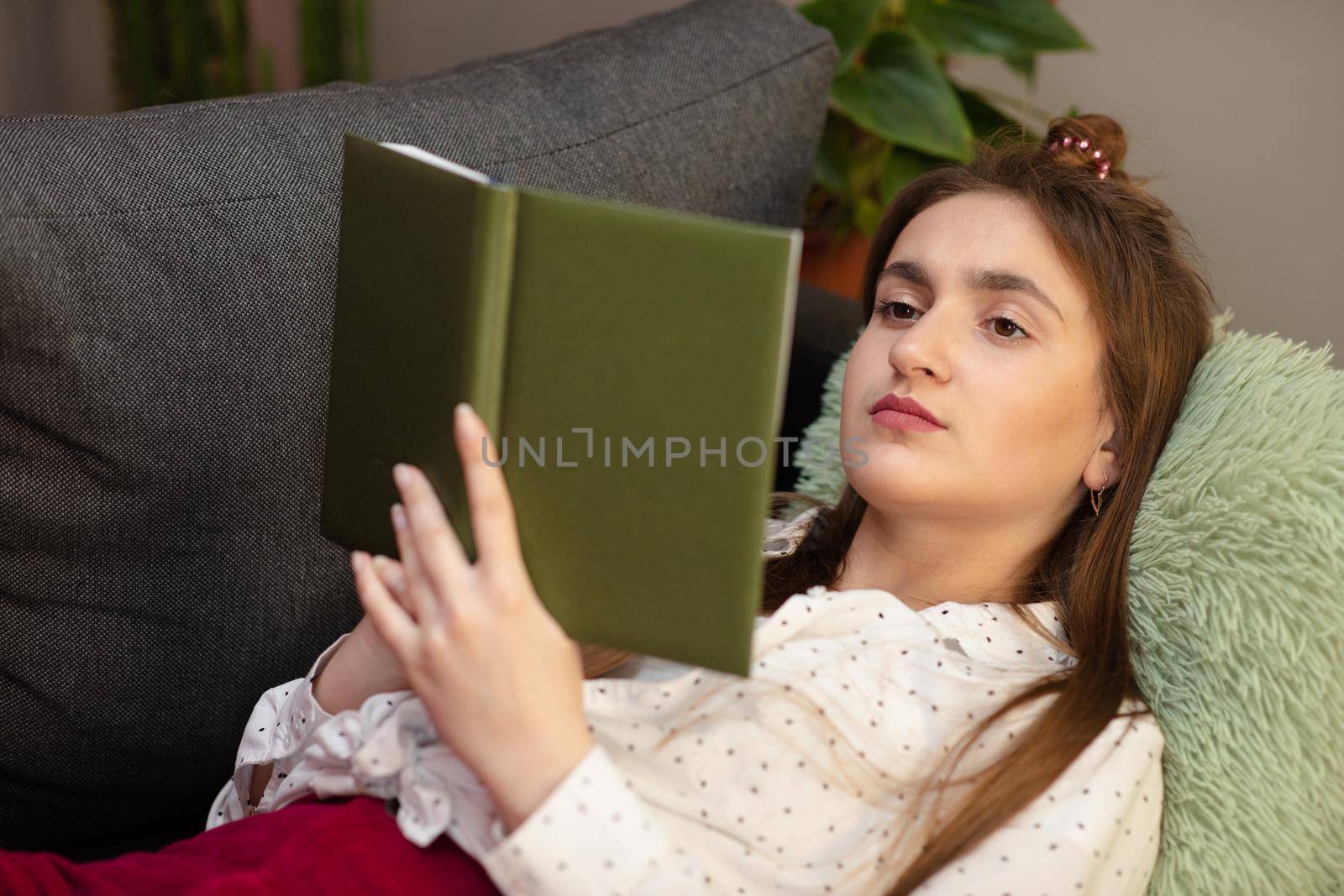 Portrait of smiling woman holding book and lying on couch. Teenager girl home - student read book laying on sofa by uflypro