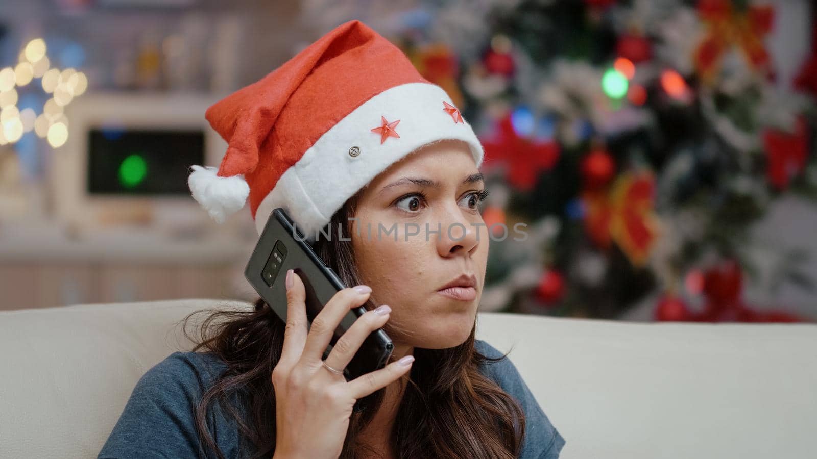 Close up of stressed person talking on smartphone for business meeting. Irritated woman with santa hat using phone call for work on christmas eve. Adult working on winter holiday