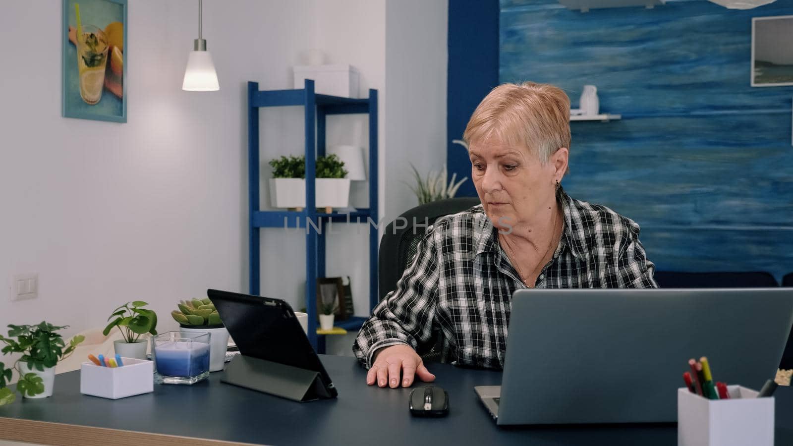 Mature woman using tablet and laptop in same time analysing financial graphs by DCStudio