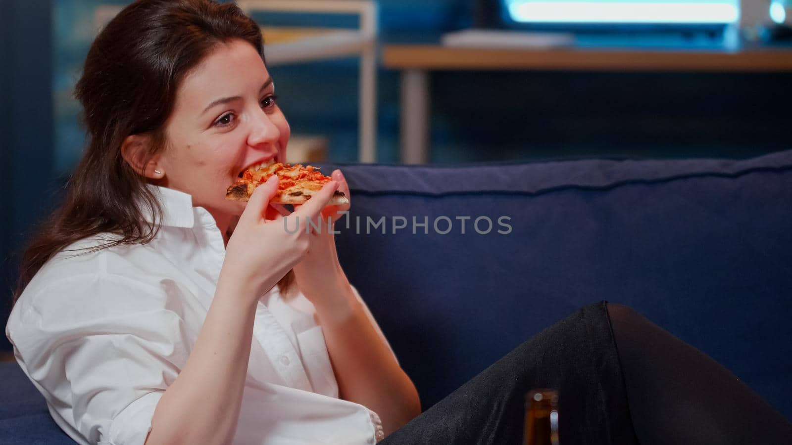 Young adult enjoying slice of pizza and beer sitting on sofa by DCStudio