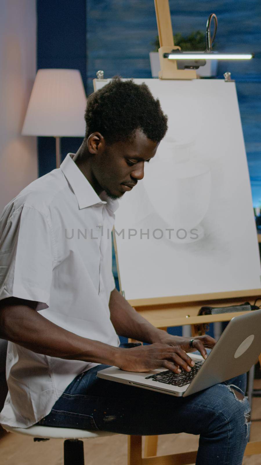 African american artist man searching inspiration on laptop computer sitting in studio space. Black young creative adult working on drawing with online technology for next masterpiece