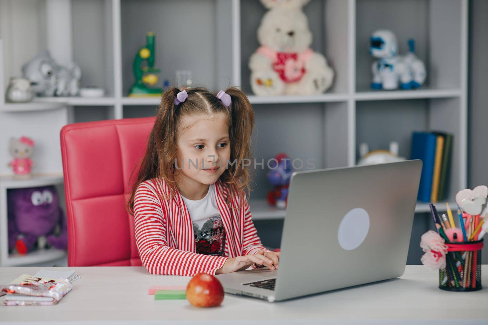 Pretty girl distance learning at home. Focused cute kid listening audio lesson studying at table, doing homework. Children remote education on quarantine concept.