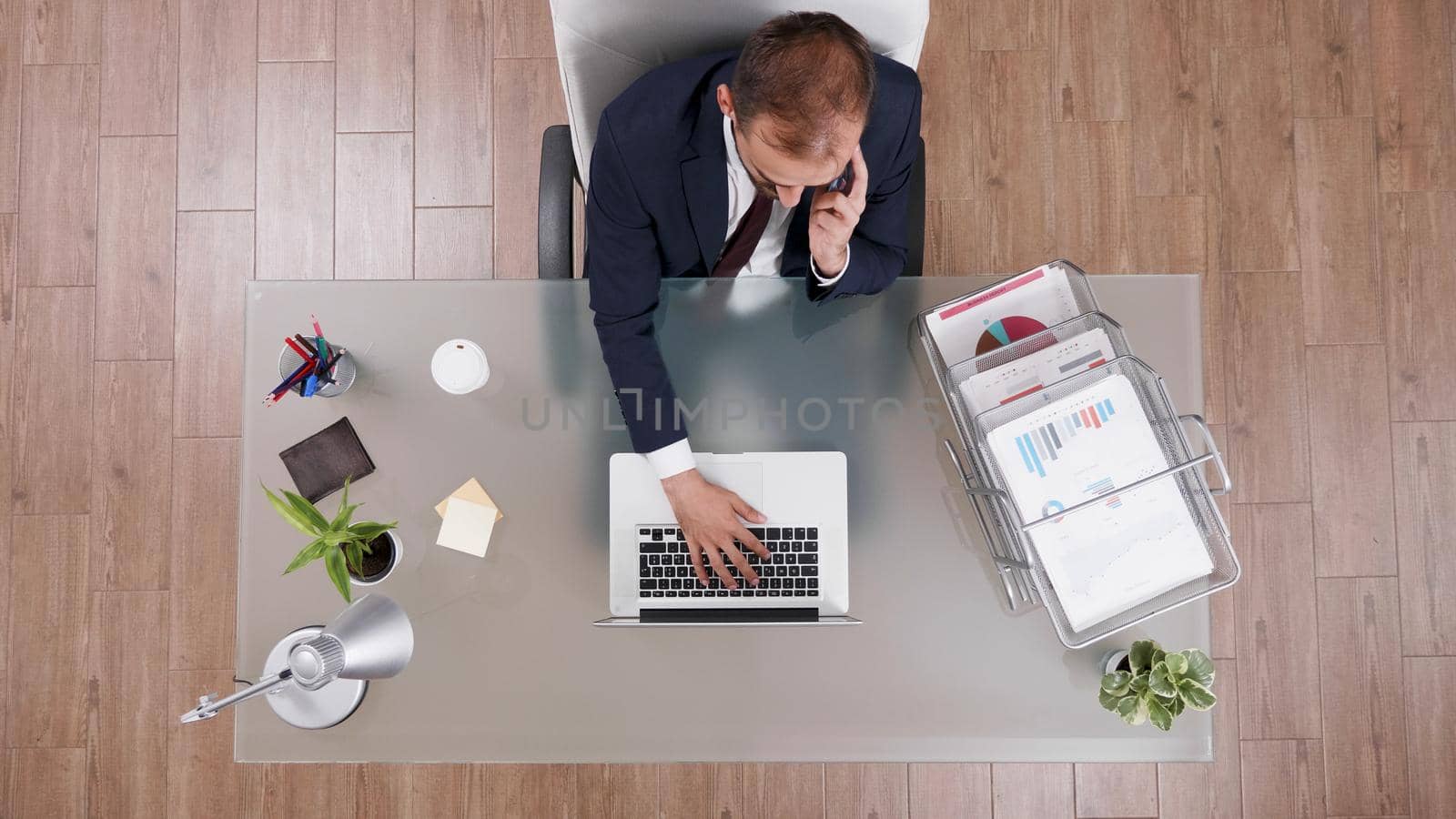 Top view of businessman discussing business profit with partner at phone while typing company statistics by DCStudio