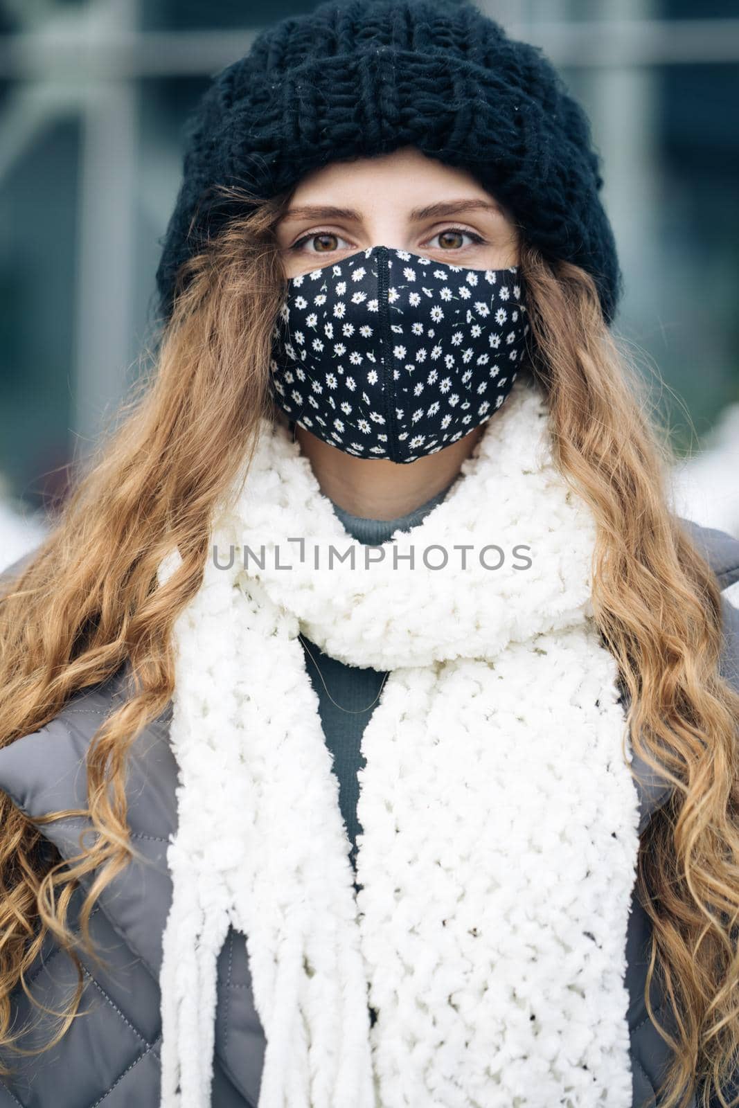 Portrait of a woman with brown curly hair out and about in the city streets during the day, wearing a face mask against air pollution and Coronavirus Covid19, looking at camera