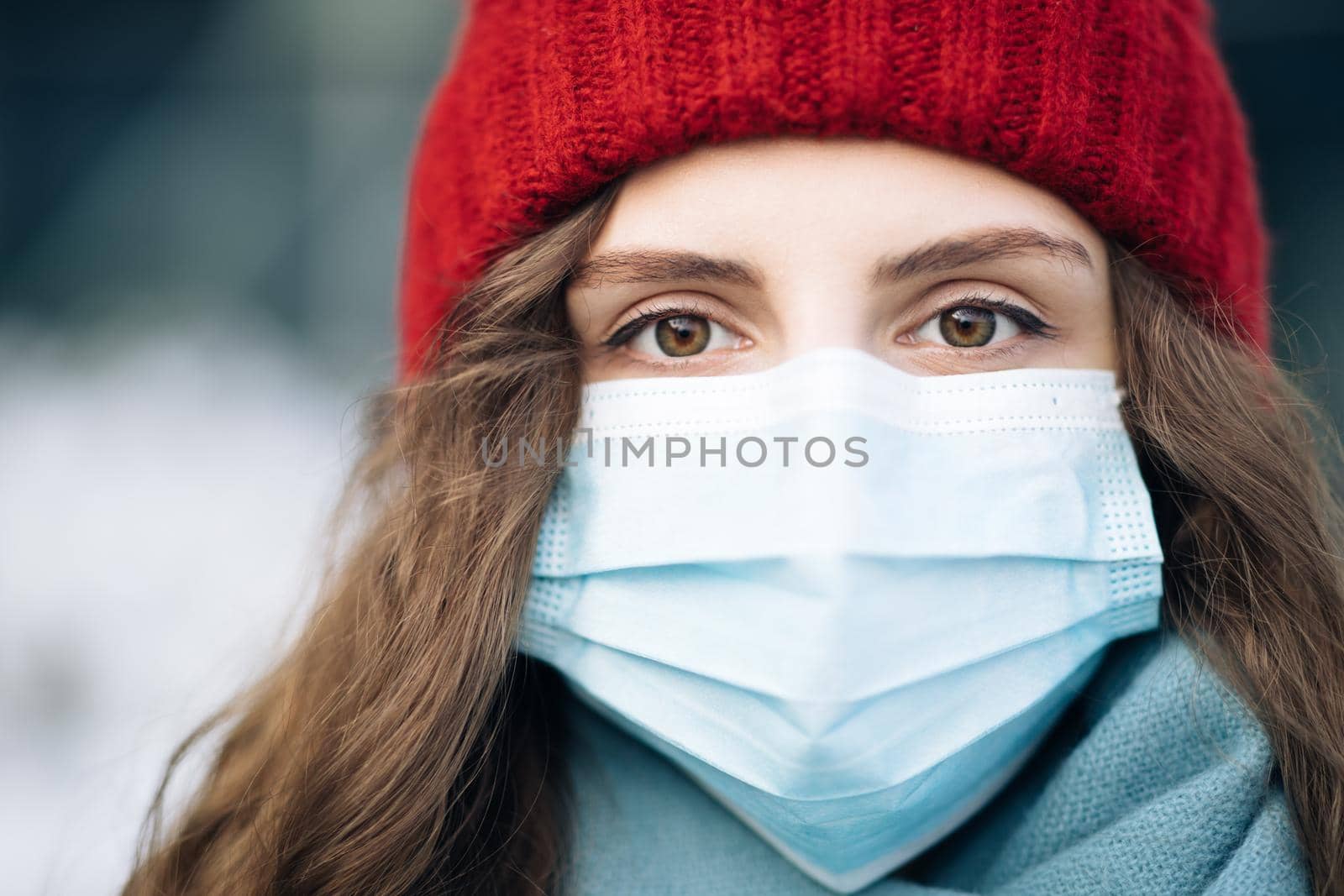 Close up of face calm serious curly haired woman wears protective mask to avoid contaminating coronavirus looks of city background. Health and safety concept. Curly female standing on winter street.