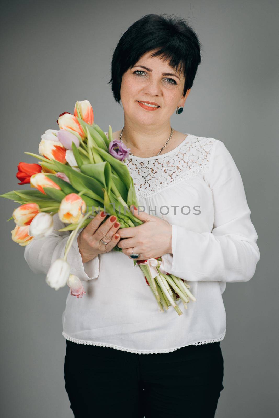 Attractive woman holds bouquet of flowers tulips in her hands gift soft toy looking at camera and smiling. Woman with tulip bouquet. Woman with gifts. by uflypro