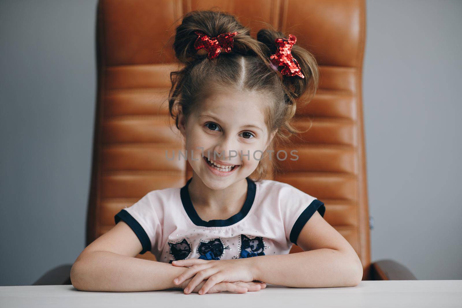 Smiling portrait of Girl Sitting at a Desk. Portrait of nice lovely attractive cheerful cheery girl sitting in chair isolated over bright vivid shine grey background