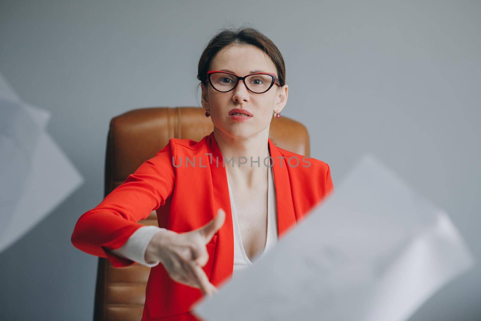 Young stressed woman sitting at desk in a little office or home mad at work, ripping documents with frustrated facial expression. Throwing around scraps of paper. Negative human emotions