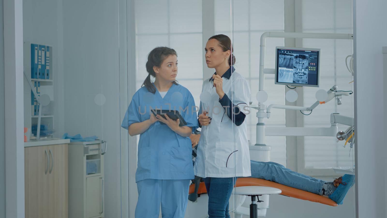 Professional dentist talking to nurse and looking at digital tablet by DCStudio