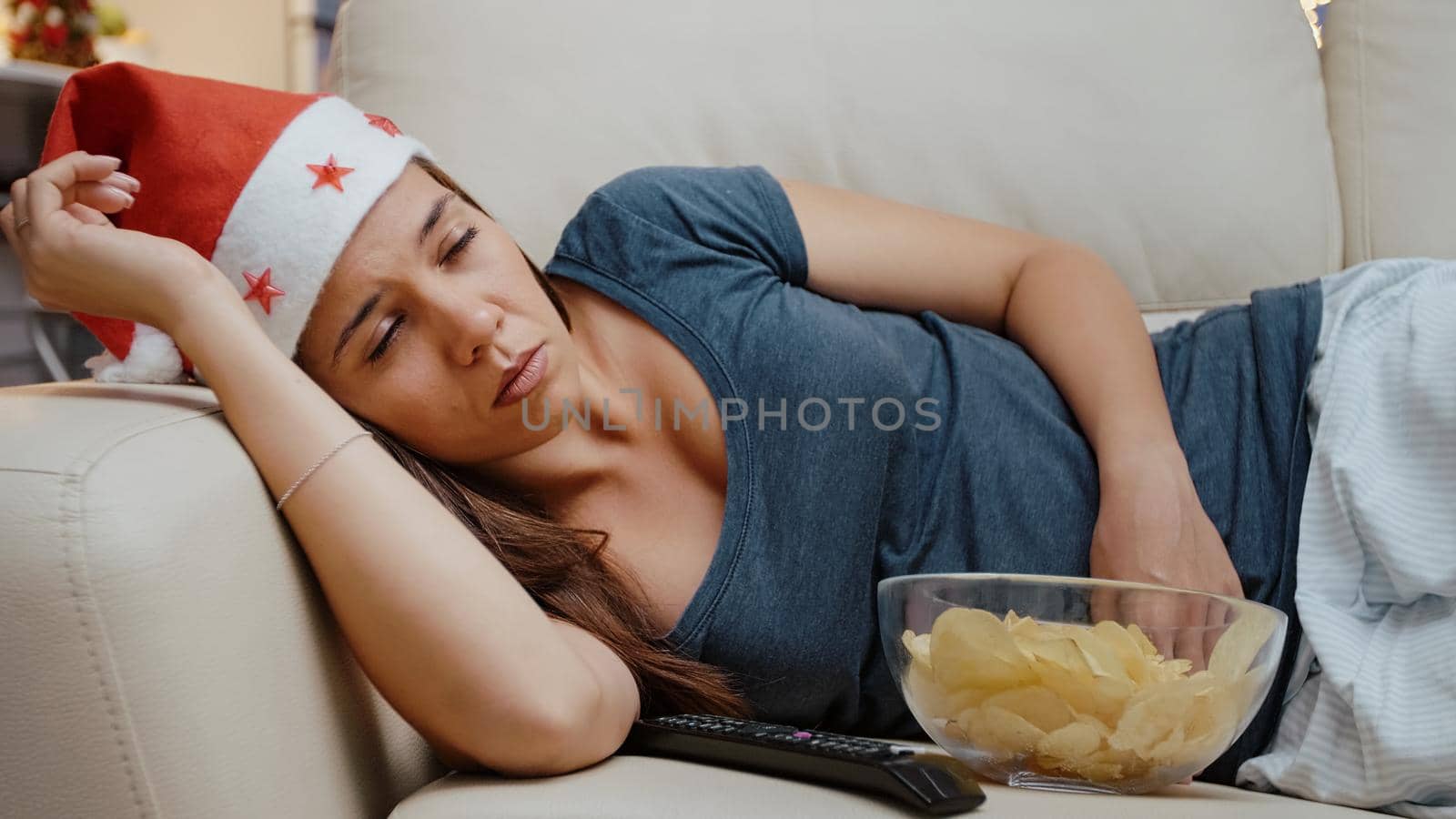 Sleepy person wearing santa hat and sitting at TV with chips by DCStudio