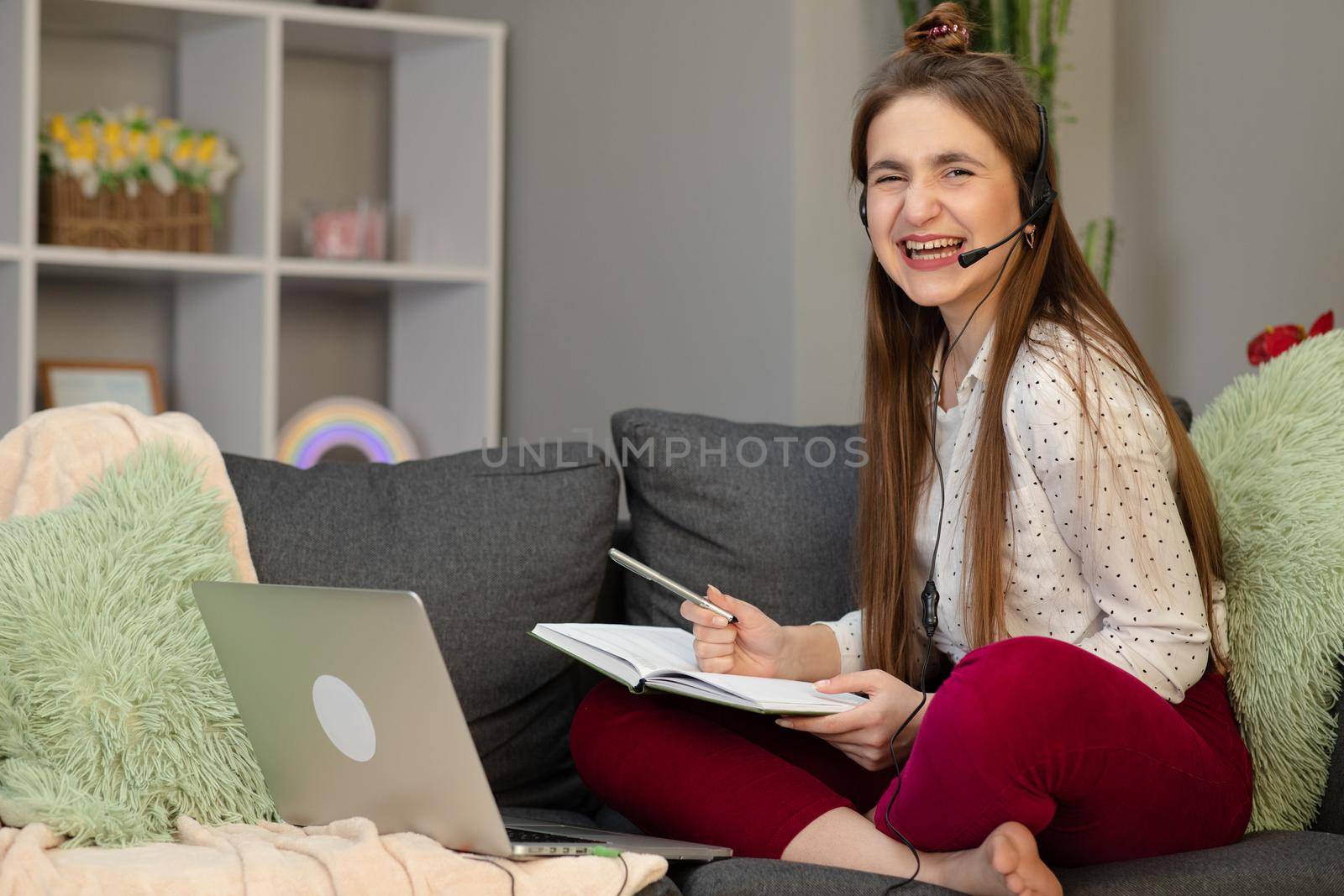 Teenage girl wearing headphones using laptop sitting on bed. Happy teen school student conference calling on computer for online distance learning communicating with friend by webcam at home by uflypro