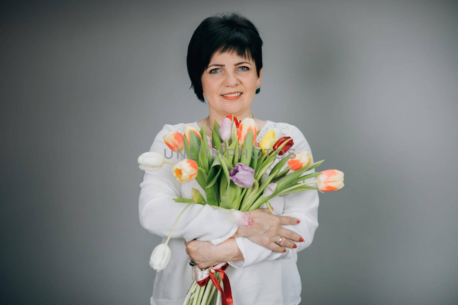 Attractive woman holds bouquet of flowers tulips in her hands gift soft toy looking at camera and smiling. Woman with tulip bouquet. Woman with gifts. by uflypro