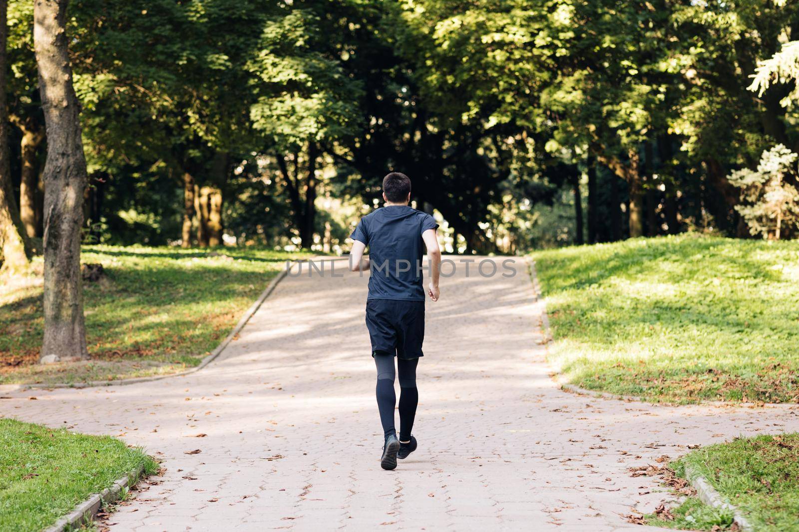 Adult man in sportswear jogging on the park in early morning. Sports people. Sportsman. Running activity. Healthy lifestyle.