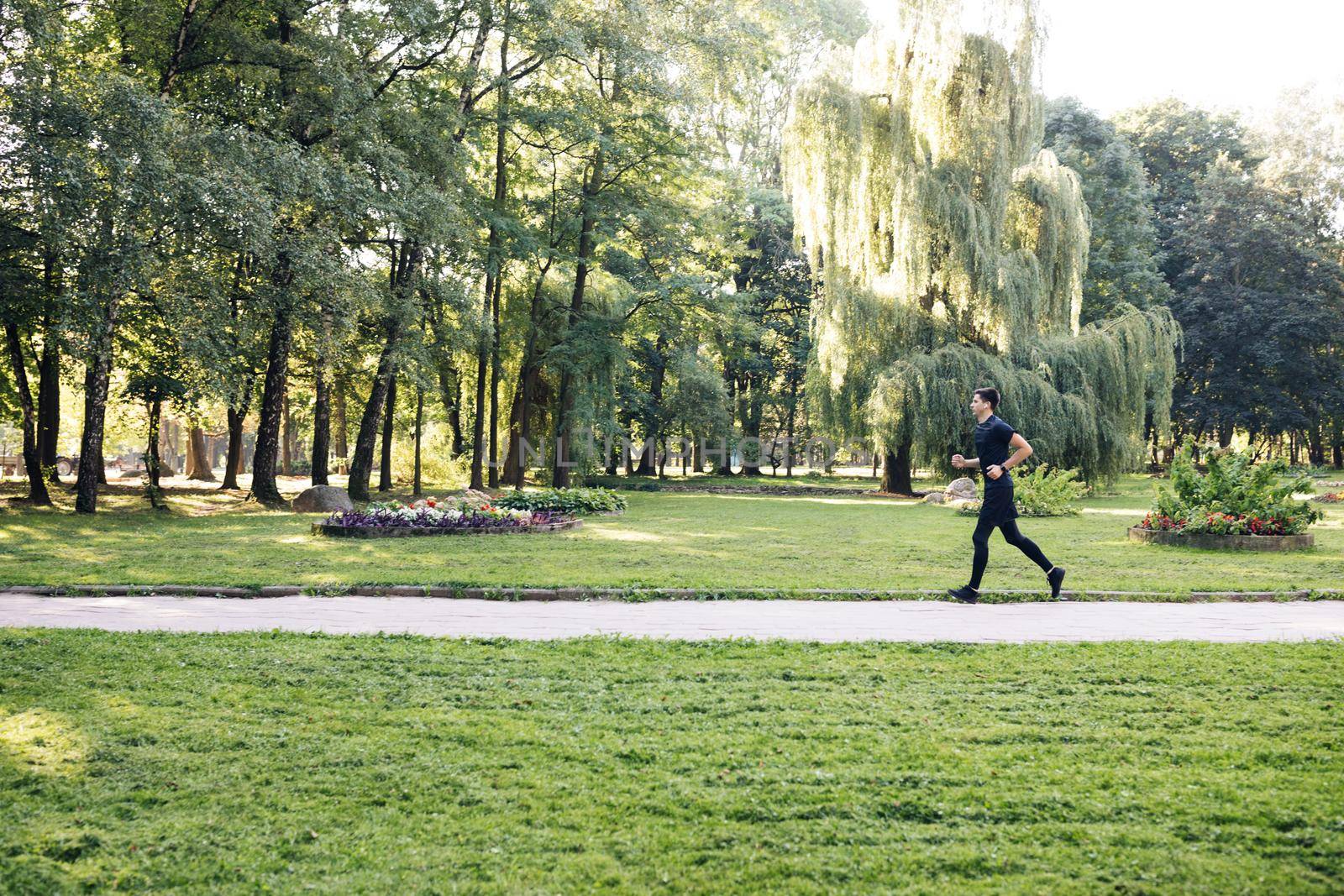 Man in summer sports uniform running in the city park with smartwatch for measuring speed, distance and heart rate. Wireless earphones. Training outside