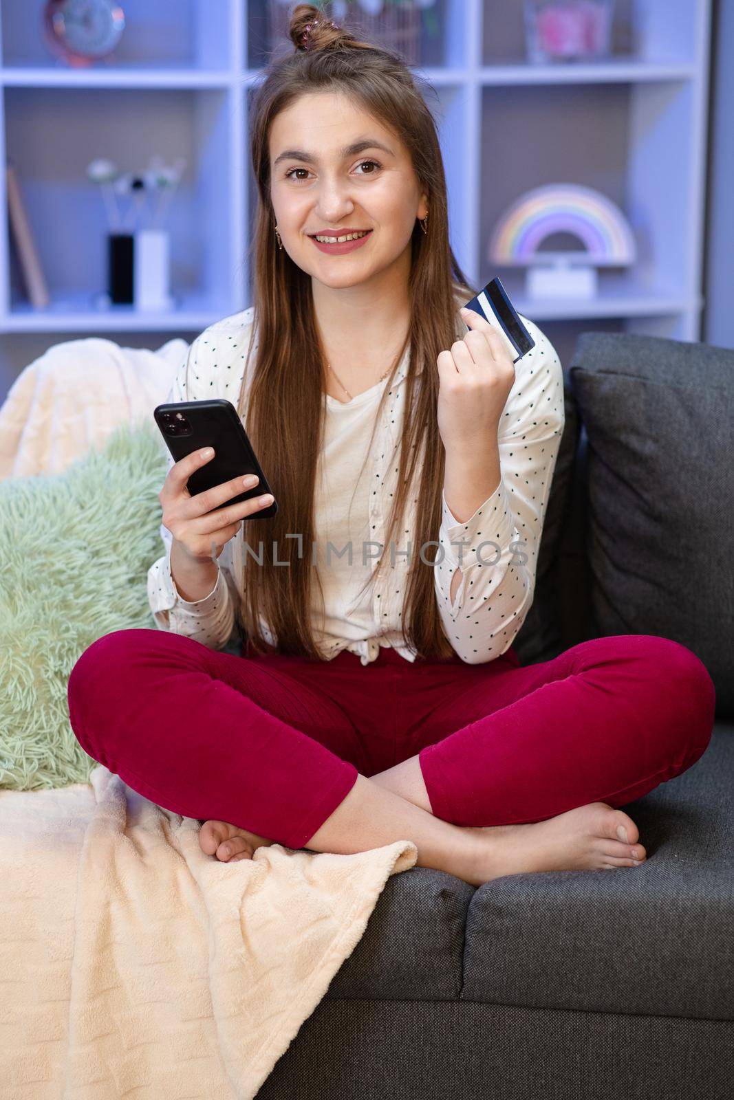 Young girl are buying online with a credit card while sitting on the sofa in the living room. Woman are using smartphone and doing online transactions.