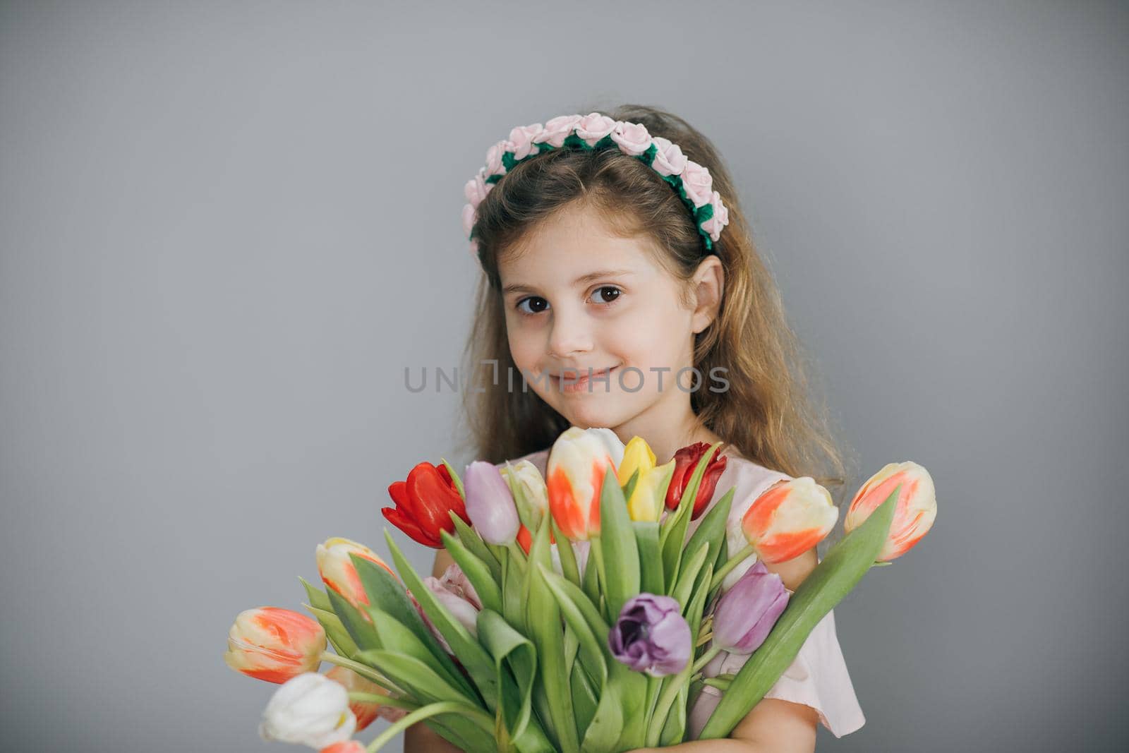 Closeup Cute girl portrait of holding flower bouquet in her hands. Model posing isolated over grey studio background. Charming female. 8 march concept. by uflypro