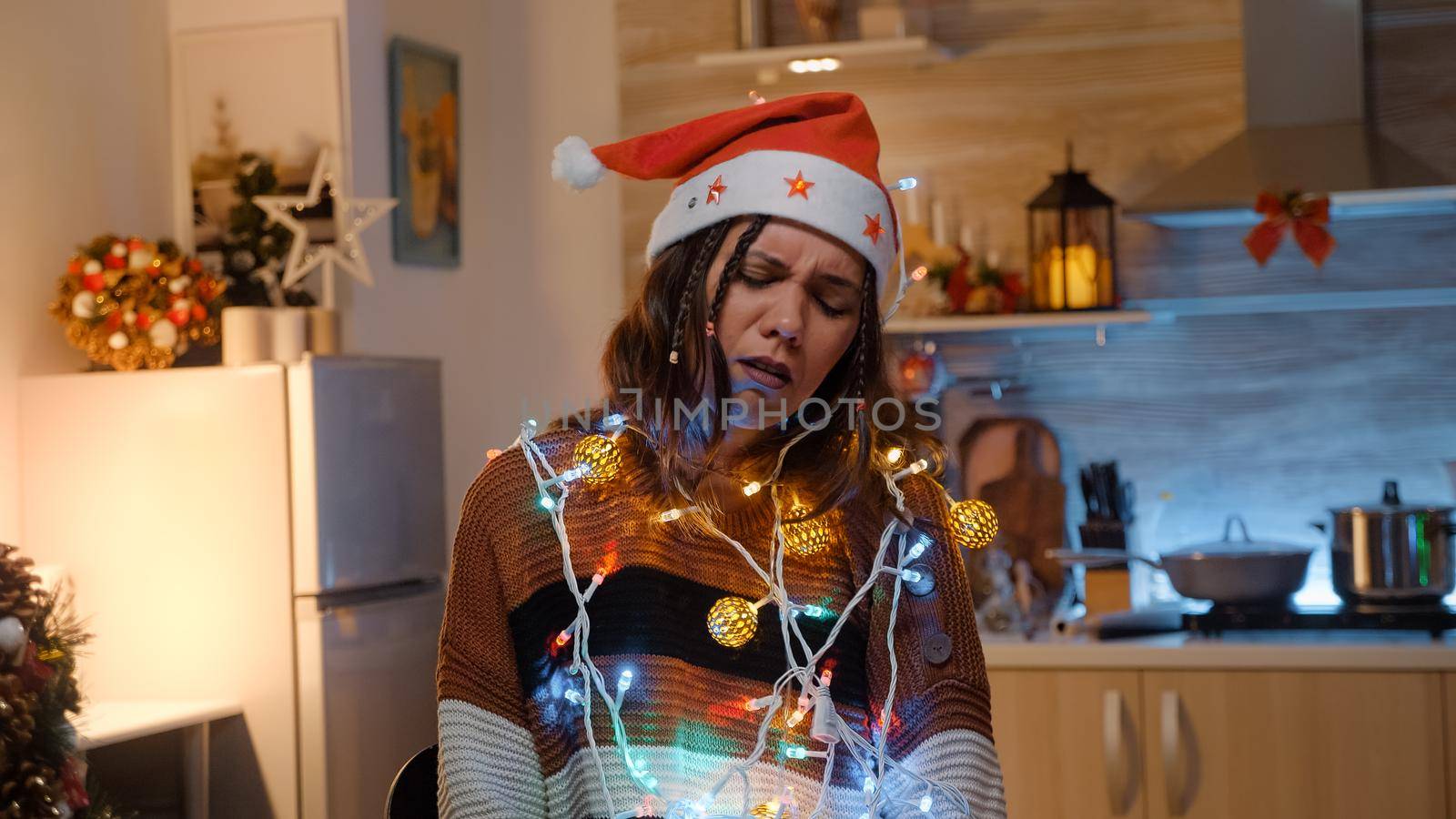 Young adult with knotted string of christmas lights tangled while trying to decorate home for winter holiday. Festive woman preparing for dinner party celebration with friends and family