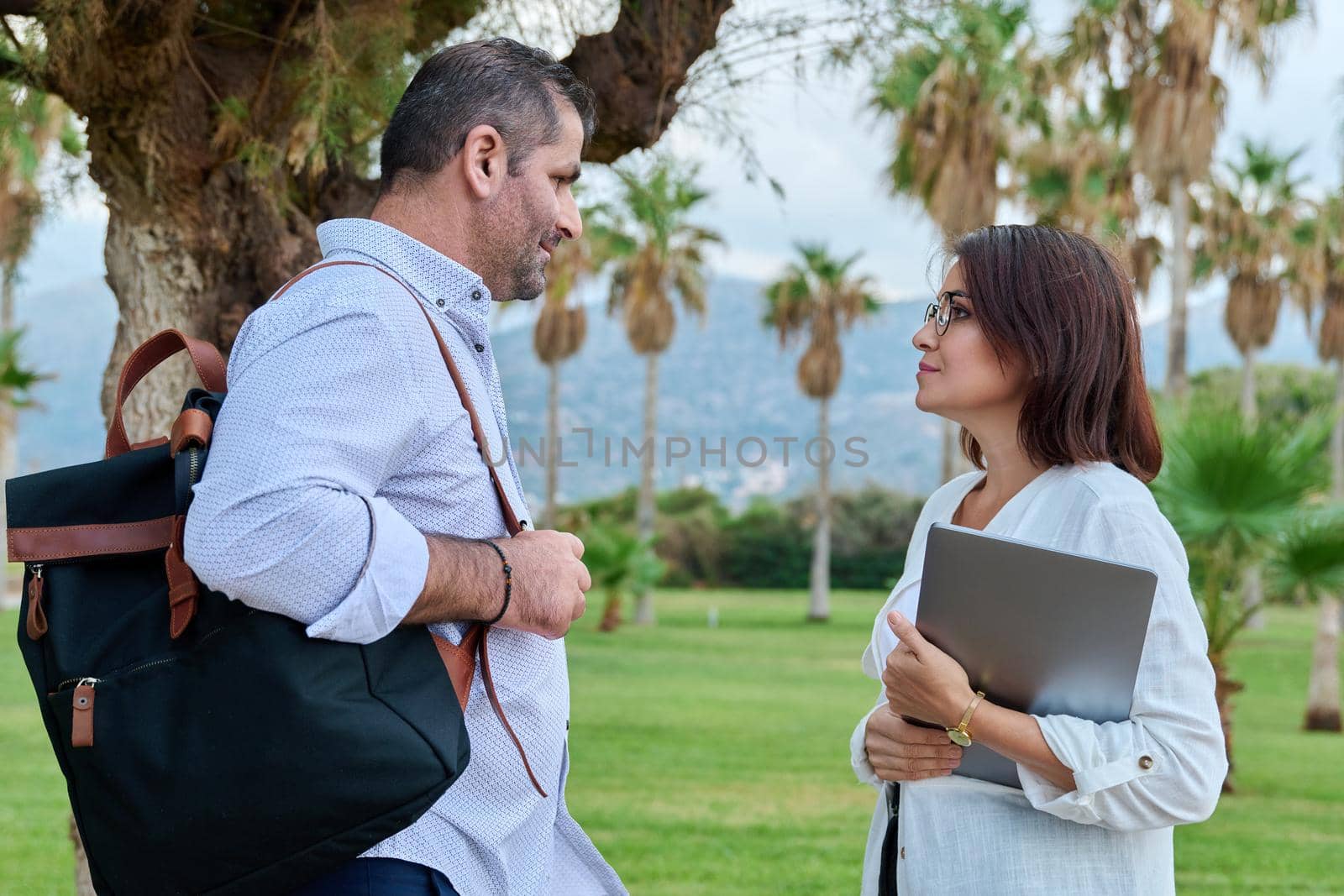 Mature man and woman business colleagues talking outdoors by VH-studio