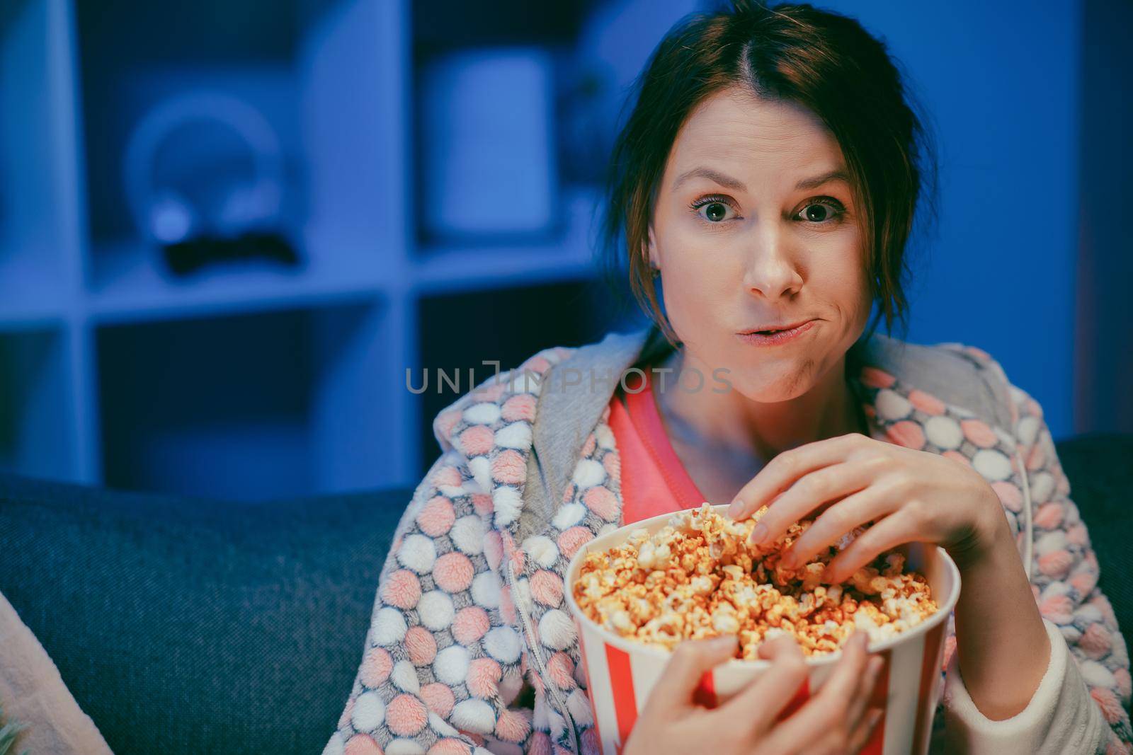 Young lady is watching TV laughing and eating popcorn having fun at home alone enjoying modern television. Youth lifestyle and cheerful people concept.