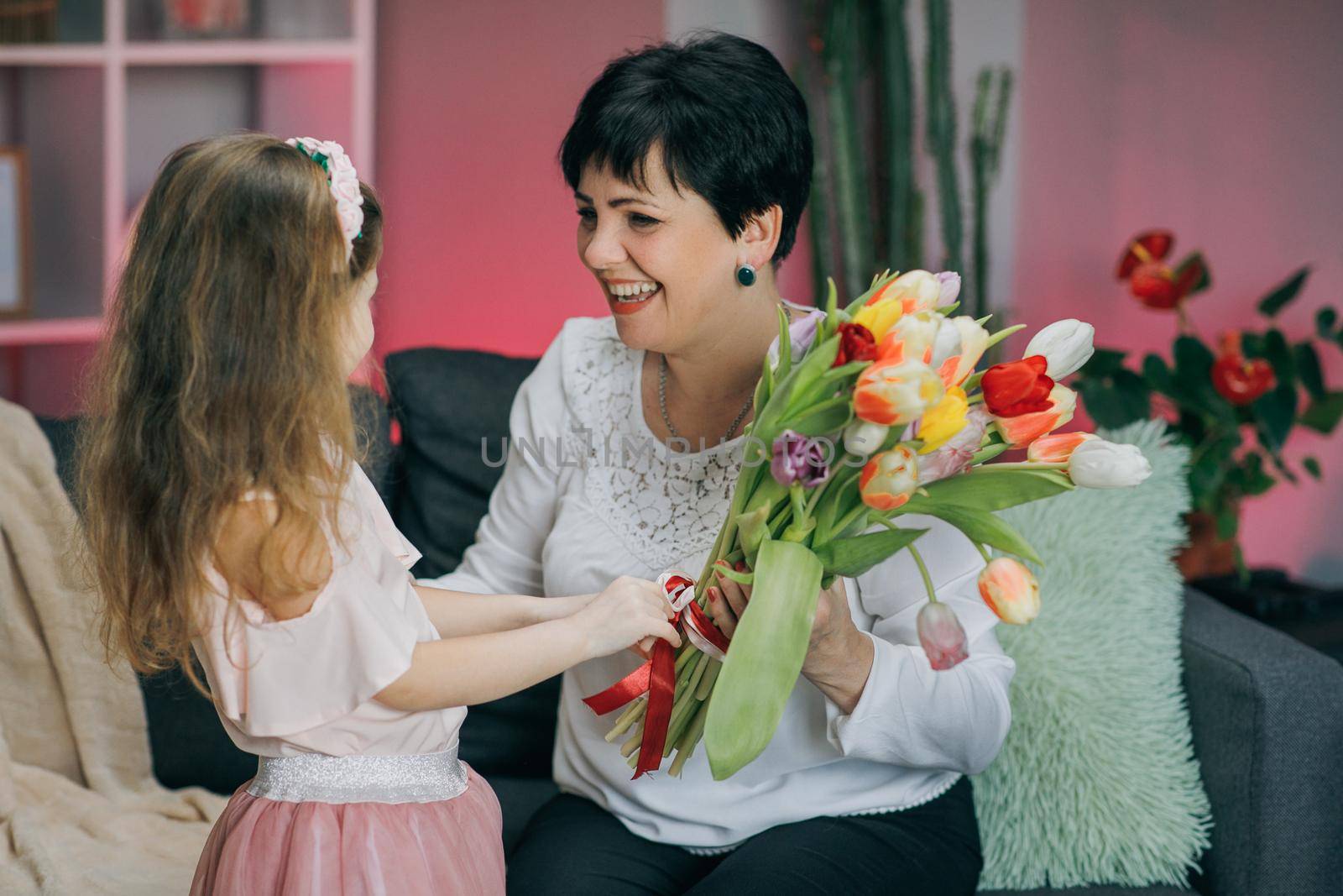 Little daughter congratulates her elderly mother on Mother's Day. A little girl hugs her mom, smiles and says gentle words to her. Kissing and hugging happy family. Happy Mother's Day. Mom and Baby.