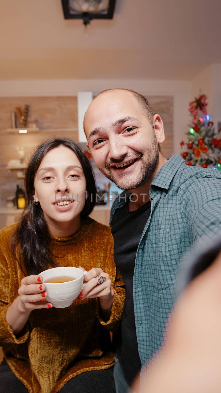 POV of festive couple talking on video call conference on christmas eve. Man and woman looking at camera smiling and chatting with relatives for holiday celebration at decorated home.