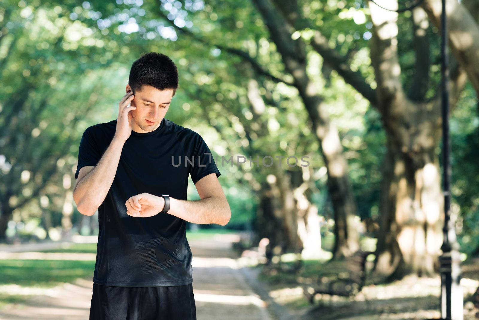 Man runner using smart watch. Handsome guy tracking result after workout. Portrait of fitness man checking result. Sport man looking smart watch by uflypro