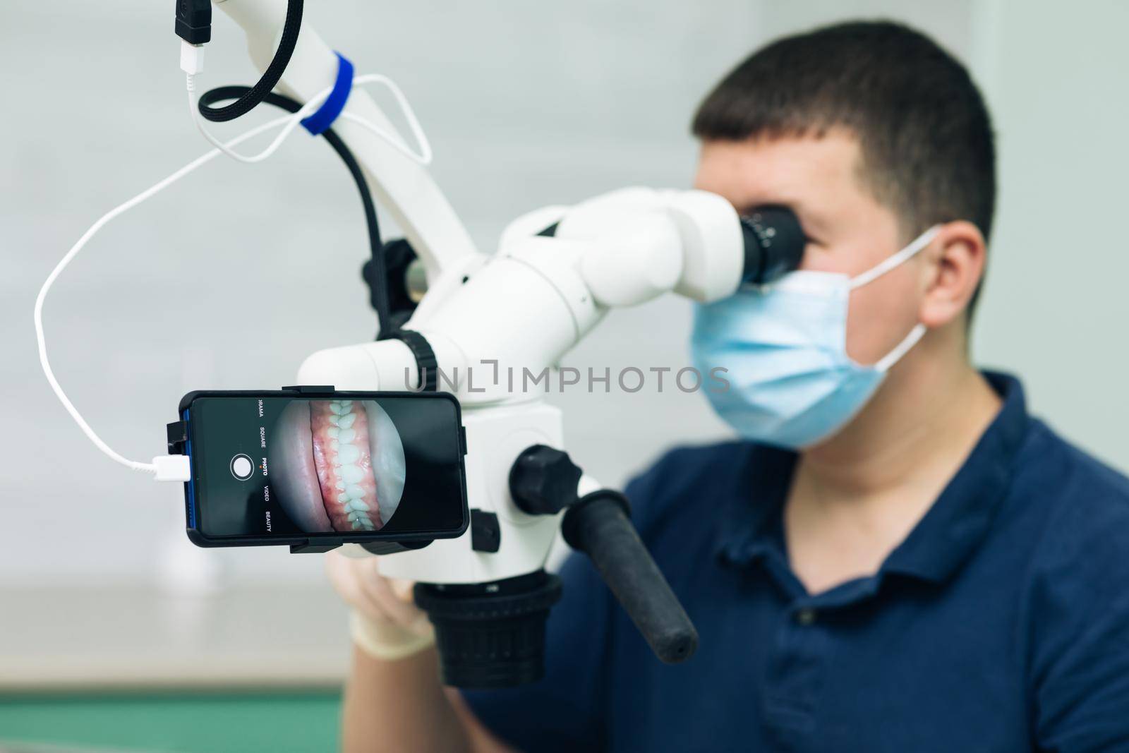 Dentist is treating patient in modern dental office. Doctor making teeth examination research survey using microscope in dentistry