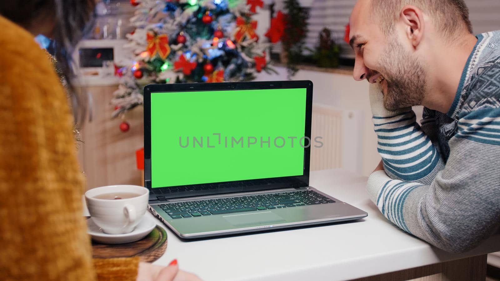 Man and woman with horizontal green screen on christmas eve looking at chroma key. Festive people watching isolated background and mockup template on seasonal holiday festivity.