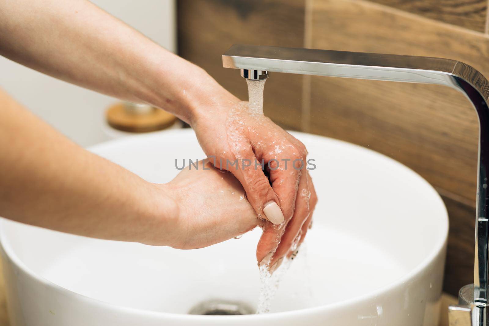 Concept of health, cleaning and preventing germs and coronavirus from contacting hands. Hands of woman wash their hands in a sink to wash the skin and water flows through the hands by uflypro
