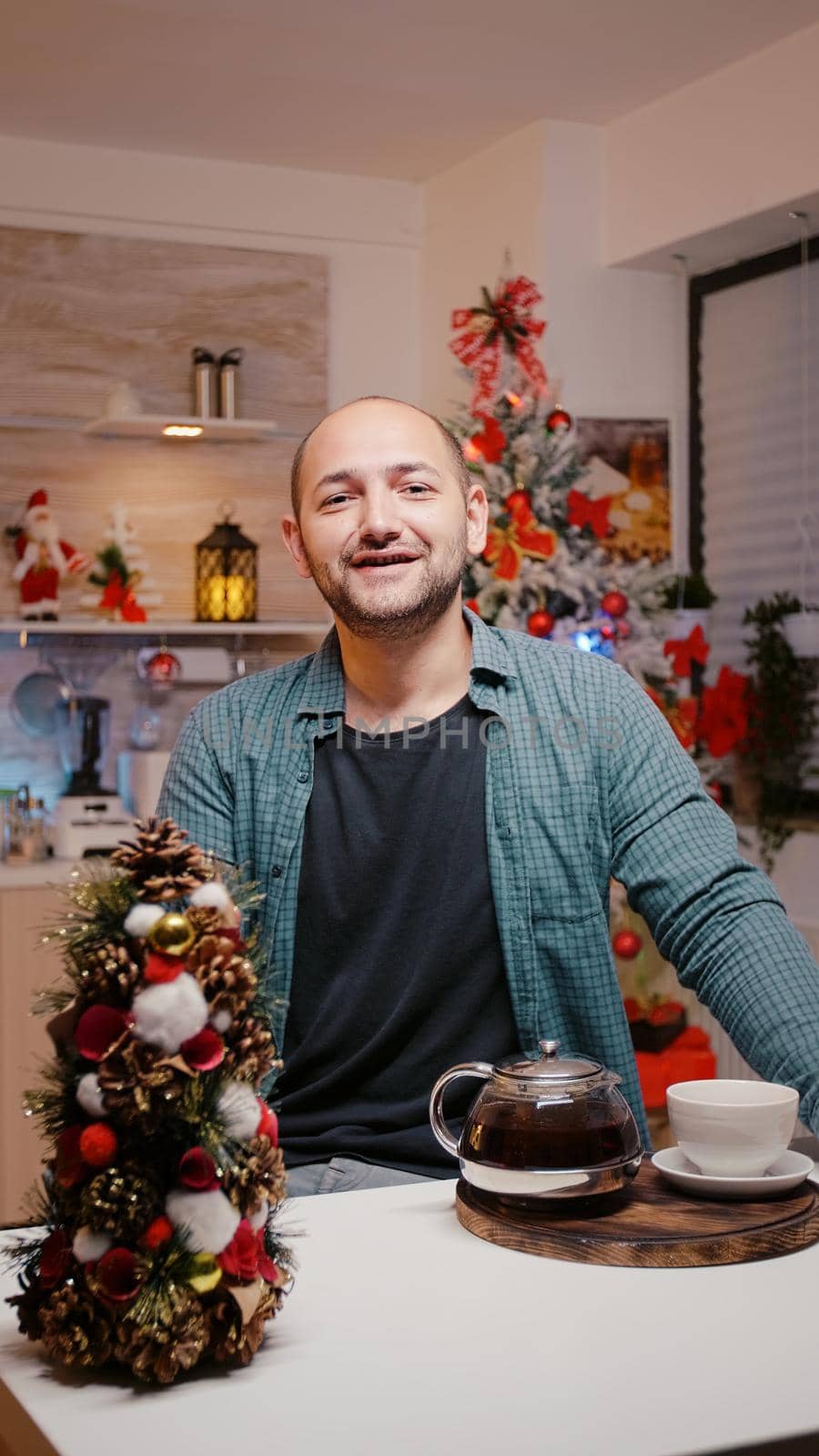 POV of man talking to family on video call conference in festive kitchen. Person looking at camera and chatting while drinking tea from cup, celebrating christmas on online communication